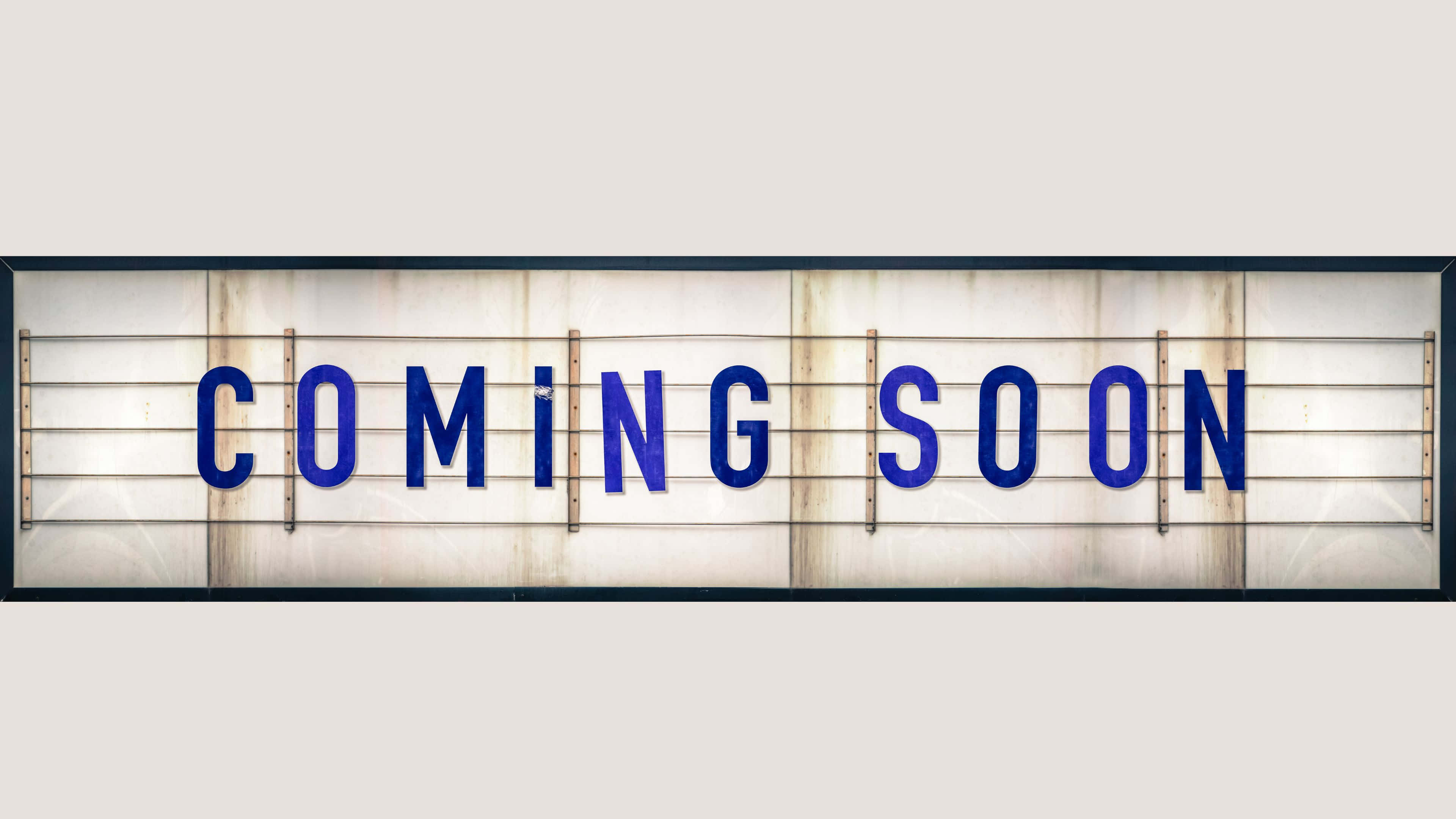 Coming Soon 桌布 壁紙 — 一個復古風格的發光招牌，以粗體藍色字母拼出「COMING SOON」，背景為經風化的白色。