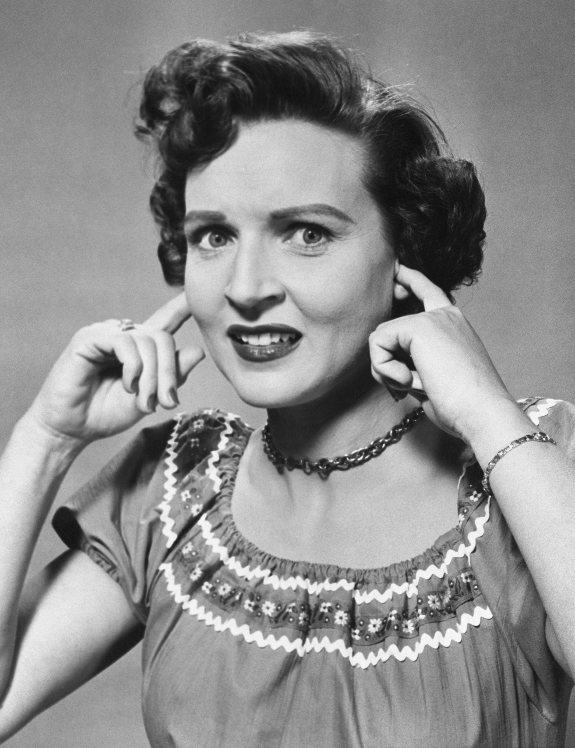 Betty White 桌布 壁紙 — 一個復古黑白肖像，一位捲髮女性微笑著抓住自己的耳朵。