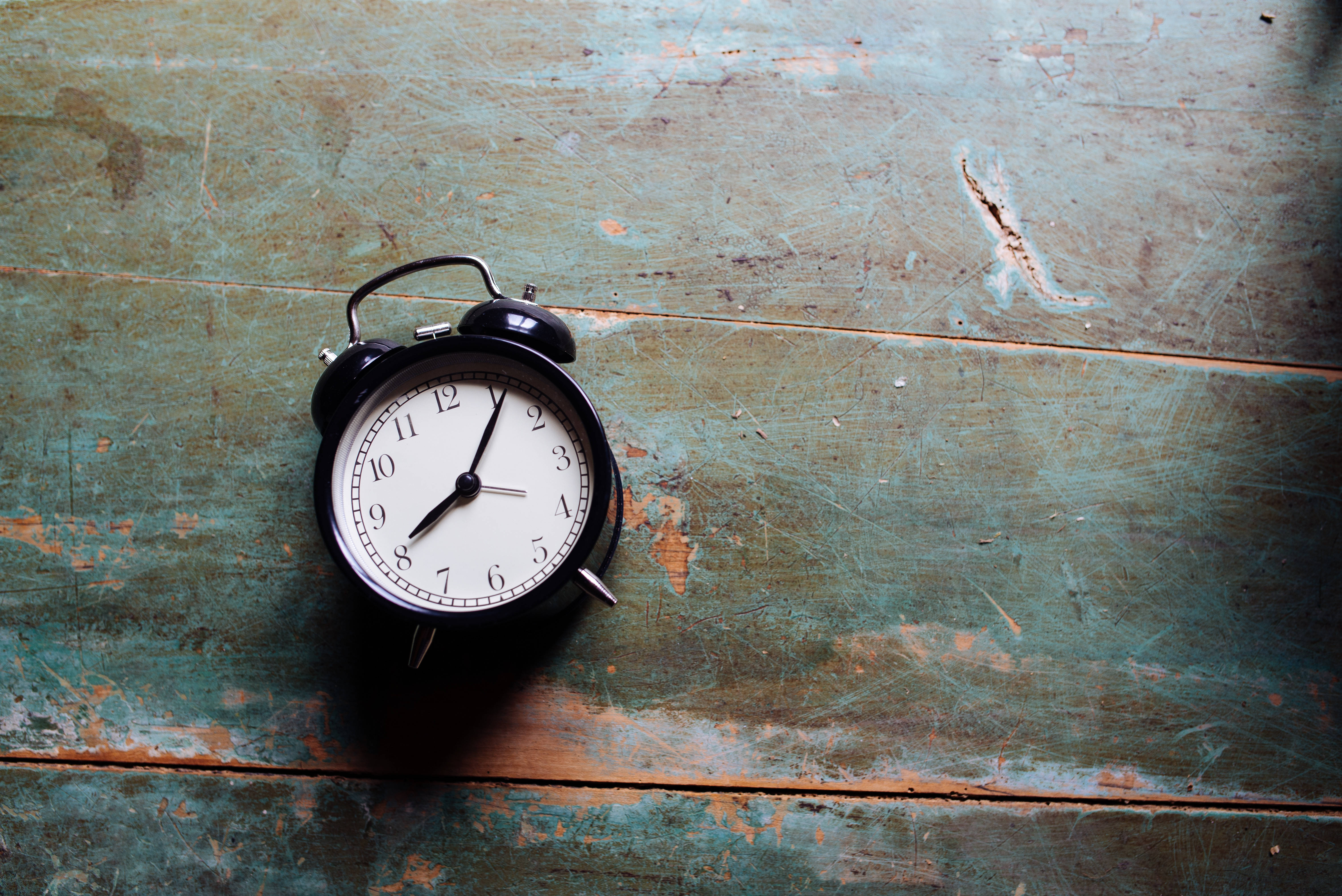 Time 桌布 壁紙 — 一個復古黑色鬧鐘放在一個經風化的青綠色木質表面上，顯示出歲月和使用痕跡。