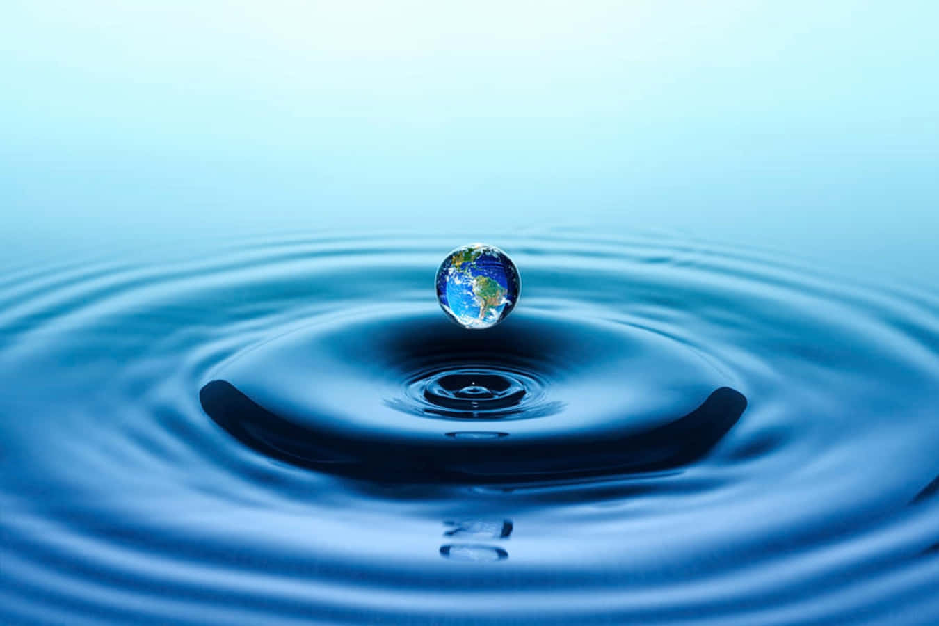 Water Drop 桌布 壁紙 — 一個微型地球儀漂浮在深藍色水中的同心漣漪上，光線柔和。