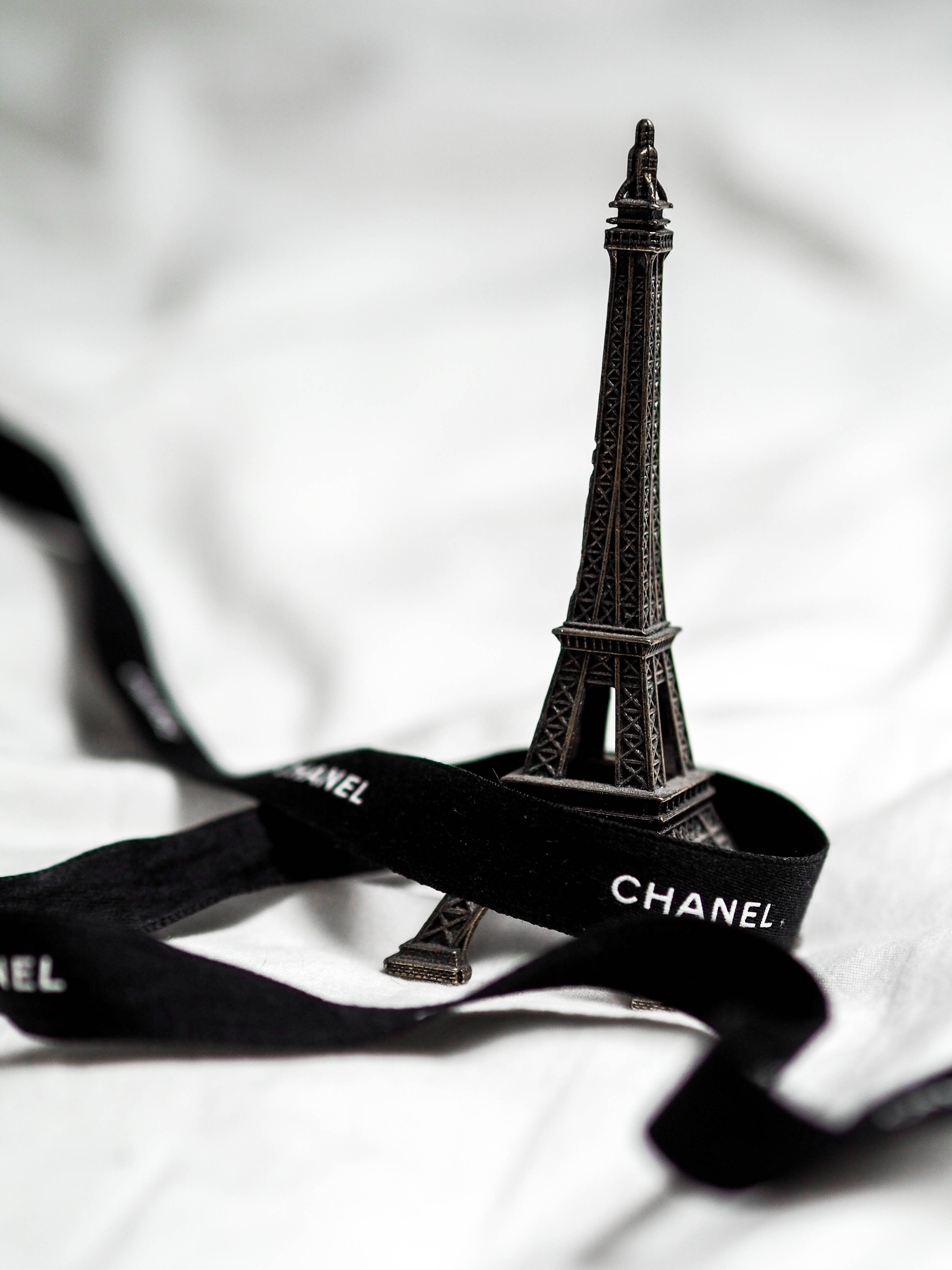 Chanel 桌布 壁紙 — 一個微型艾菲爾鐵塔模型放在黑色 Chanel 絲帶上，背景是潔白的布料。