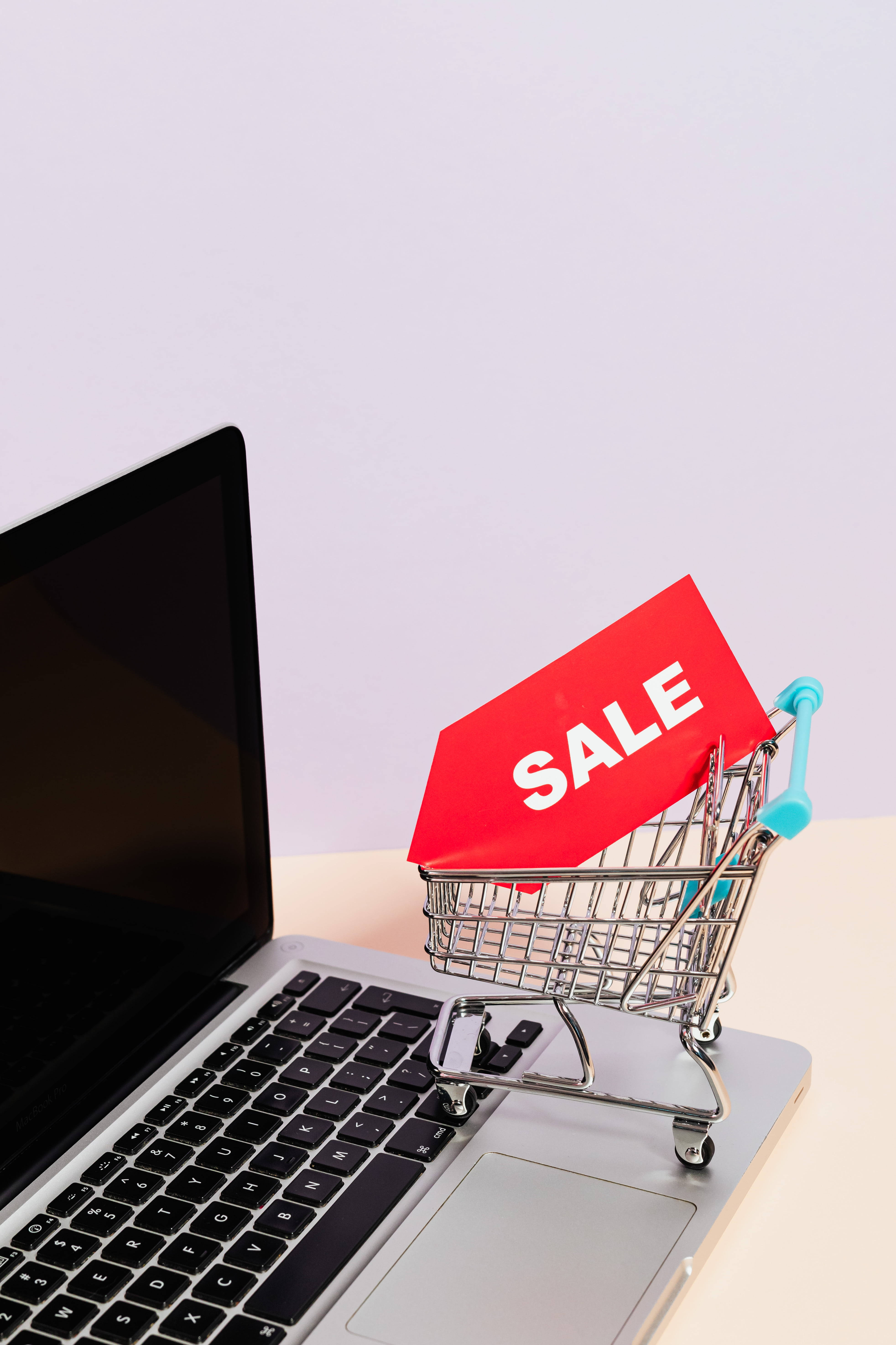 Sales 桌布 壁紙 — 一個微型購物車拿著紅色特價標誌，放在柔軟薰衣草背景的筆記型電腦鍵盤上。