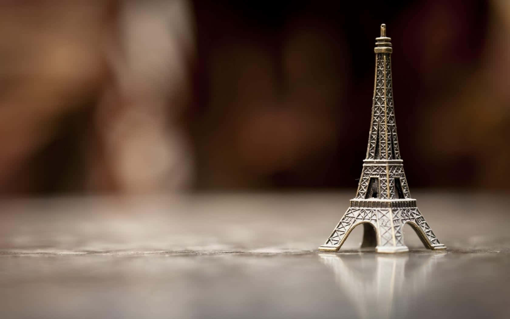 Eiffel Tower 桌布 壁紙 — 一個微型銀色艾菲爾鐵塔雕像獨自站在反射表面上，背景柔和模糊溫暖。
