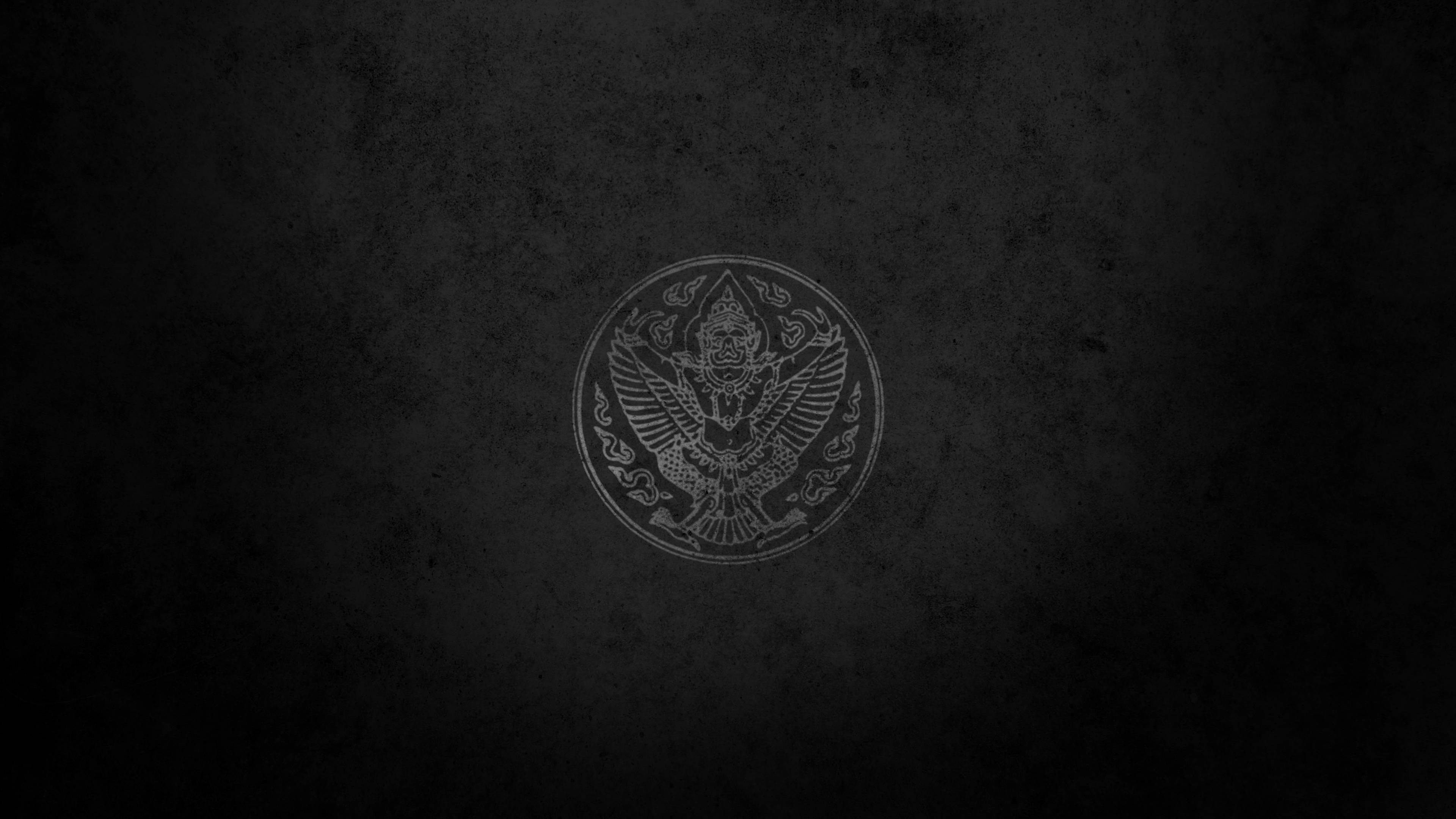 Logo 桌布 壁紙 — 一個微弱蝕刻的圓形徽章，中央是一隻展翅的皇冠鷹，位於有紋理的深灰色背景上。