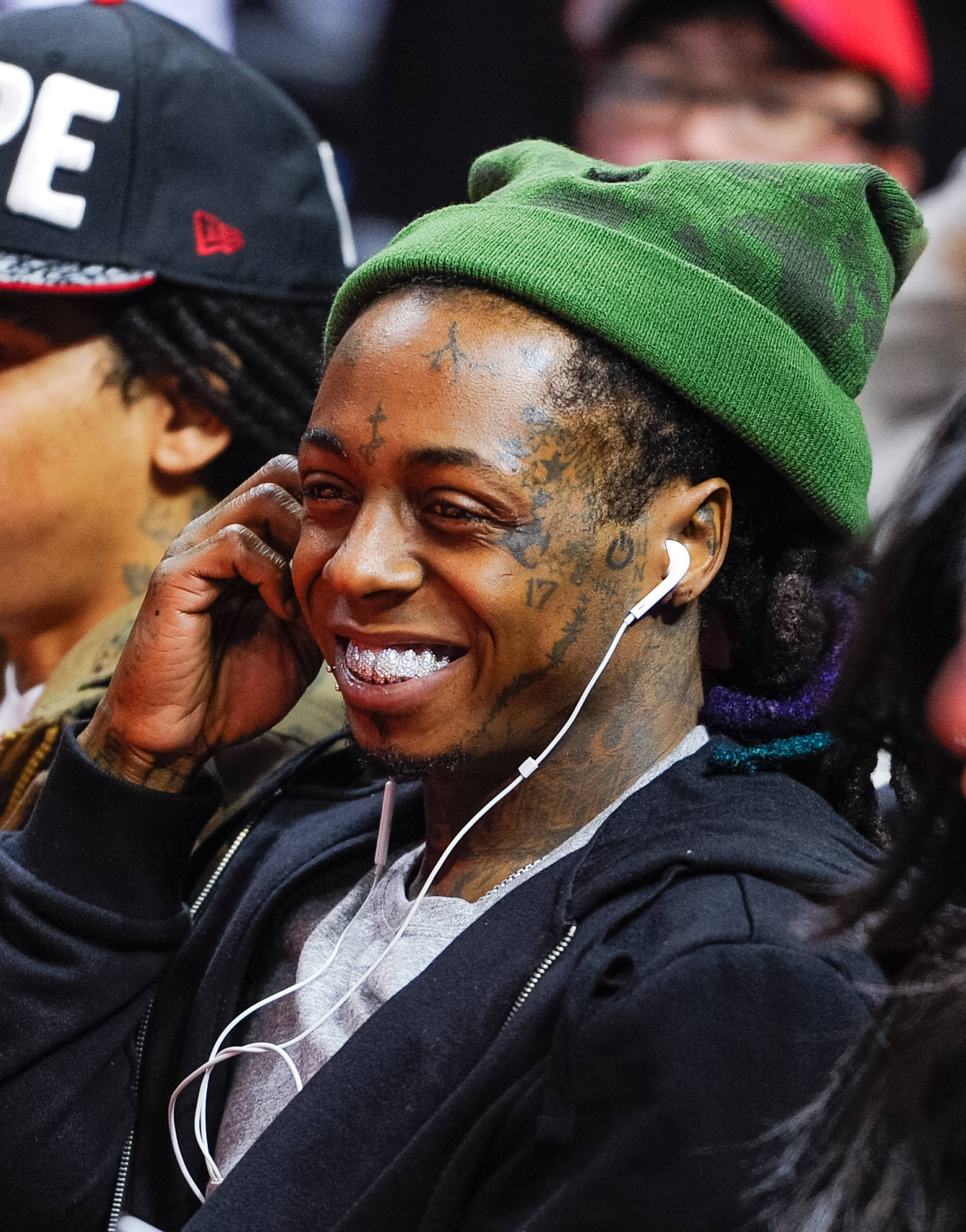 Lil Wayne 桌布 壁紙 — 一個微笑、有刺青、戴綠色毛帽的男人在擁擠的活動中用白色耳塞聽音樂。