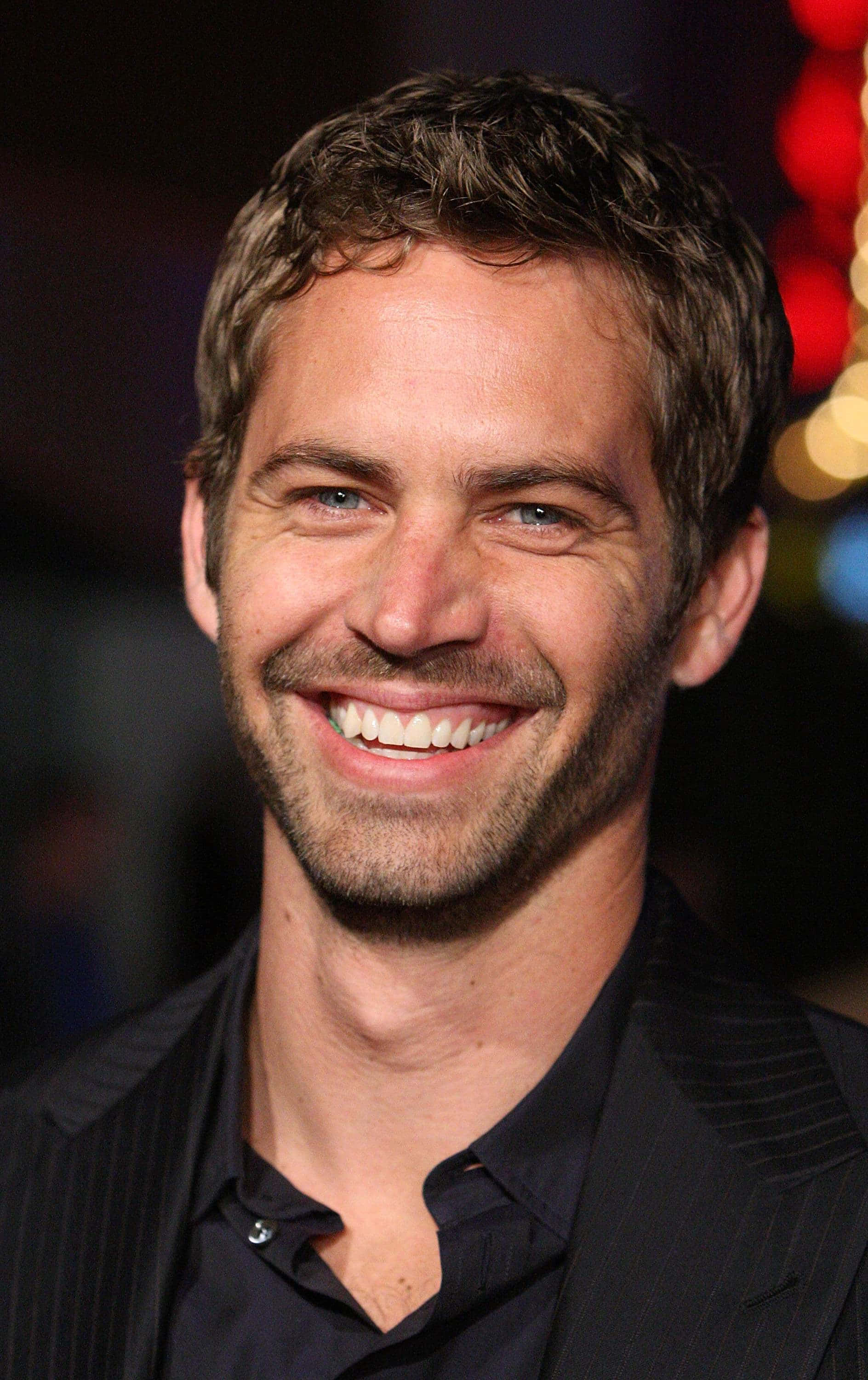 Paul Walker 桌布 壁紙 — 一個微笑男人的特寫肖像，他有藍色眼睛和鬍渣，背景是模糊多彩的散景。