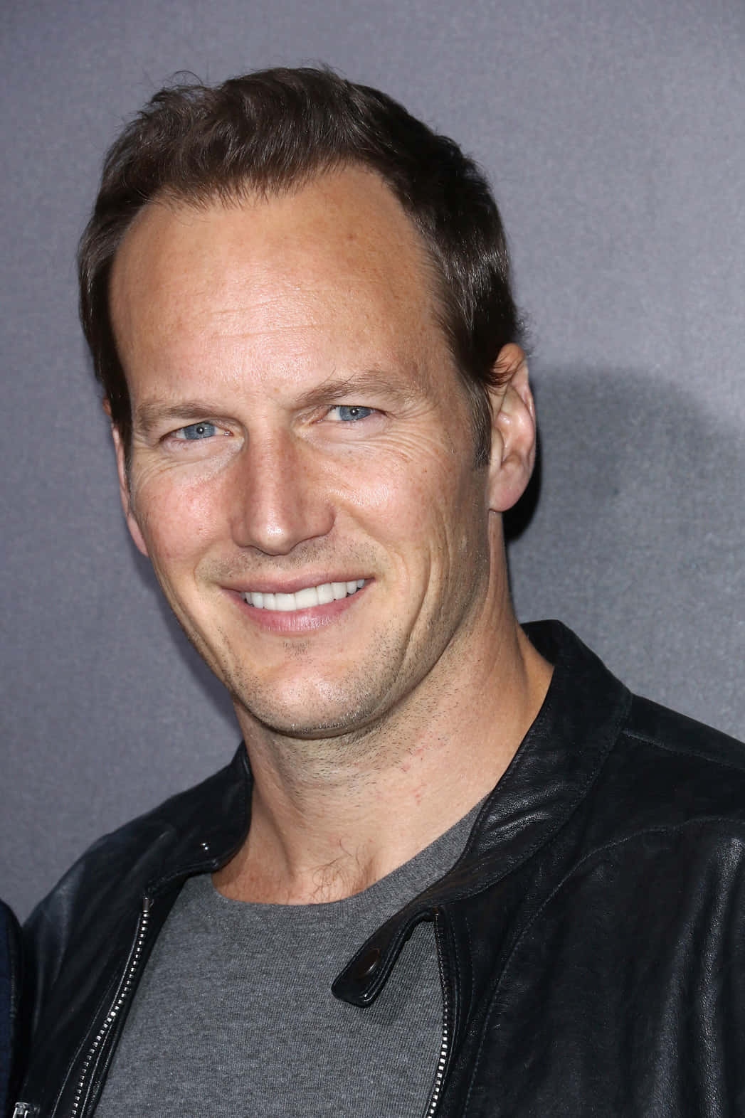 Patrick Wilson 桌布 壁紙 — 一個微笑男人的特寫肖像，他有藍色眼睛，在灰色背景前穿著一件黑色皮夾克和灰色襯衫。