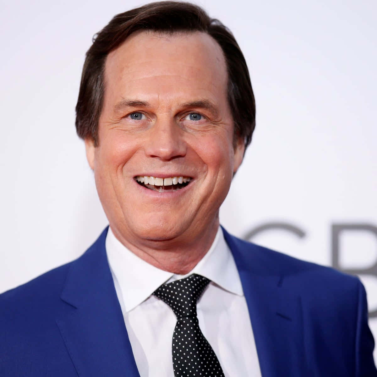 Celebrity 桌布 壁紙 — 一個微笑男士的 close-up 肖像，身穿俐落藍色西裝和波點領帶，背景為白色。