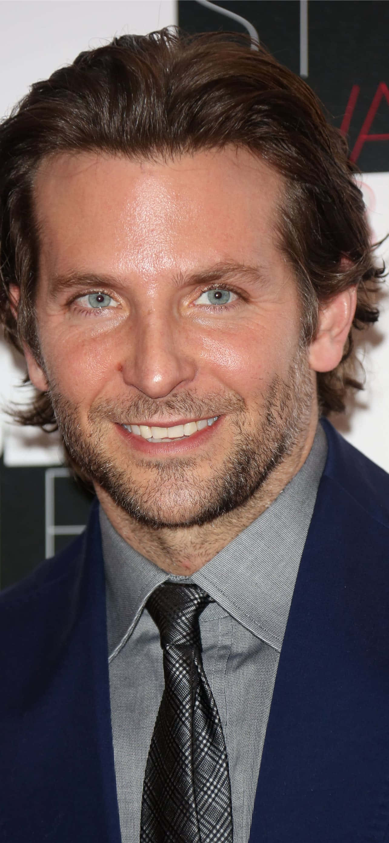 Bradley Cooper 桌布 壁紙 — 一個微笑男士的特寫肖像，藍眼睛、棕色頭髮，身穿海軍藍西裝和圖案領帶。