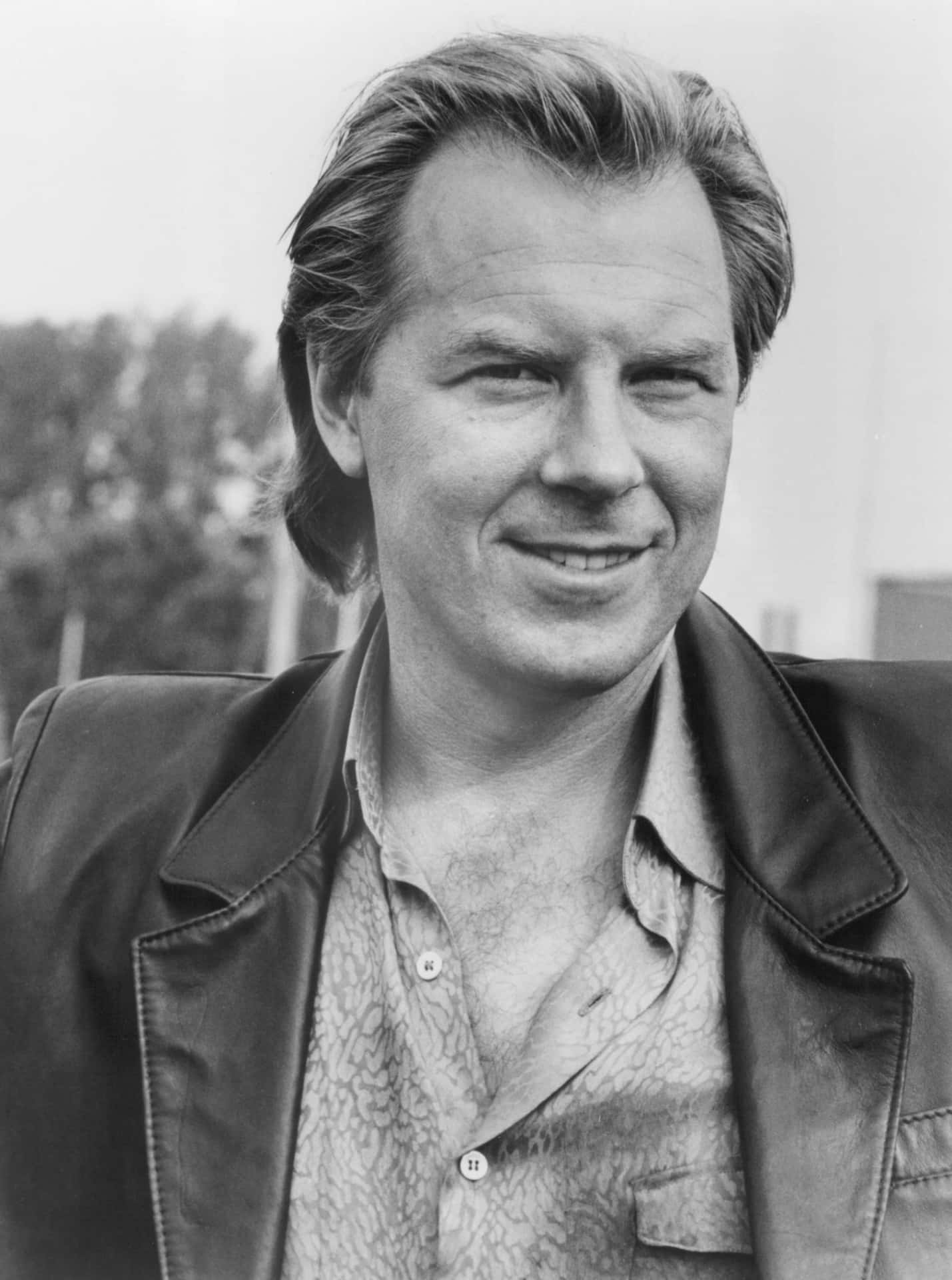 Michael Mckean 桌布 壁紙 — 一個微笑男士的黑白肖像，他梳著時尚髮型，身穿皮夾克內搭圖案襯衫。