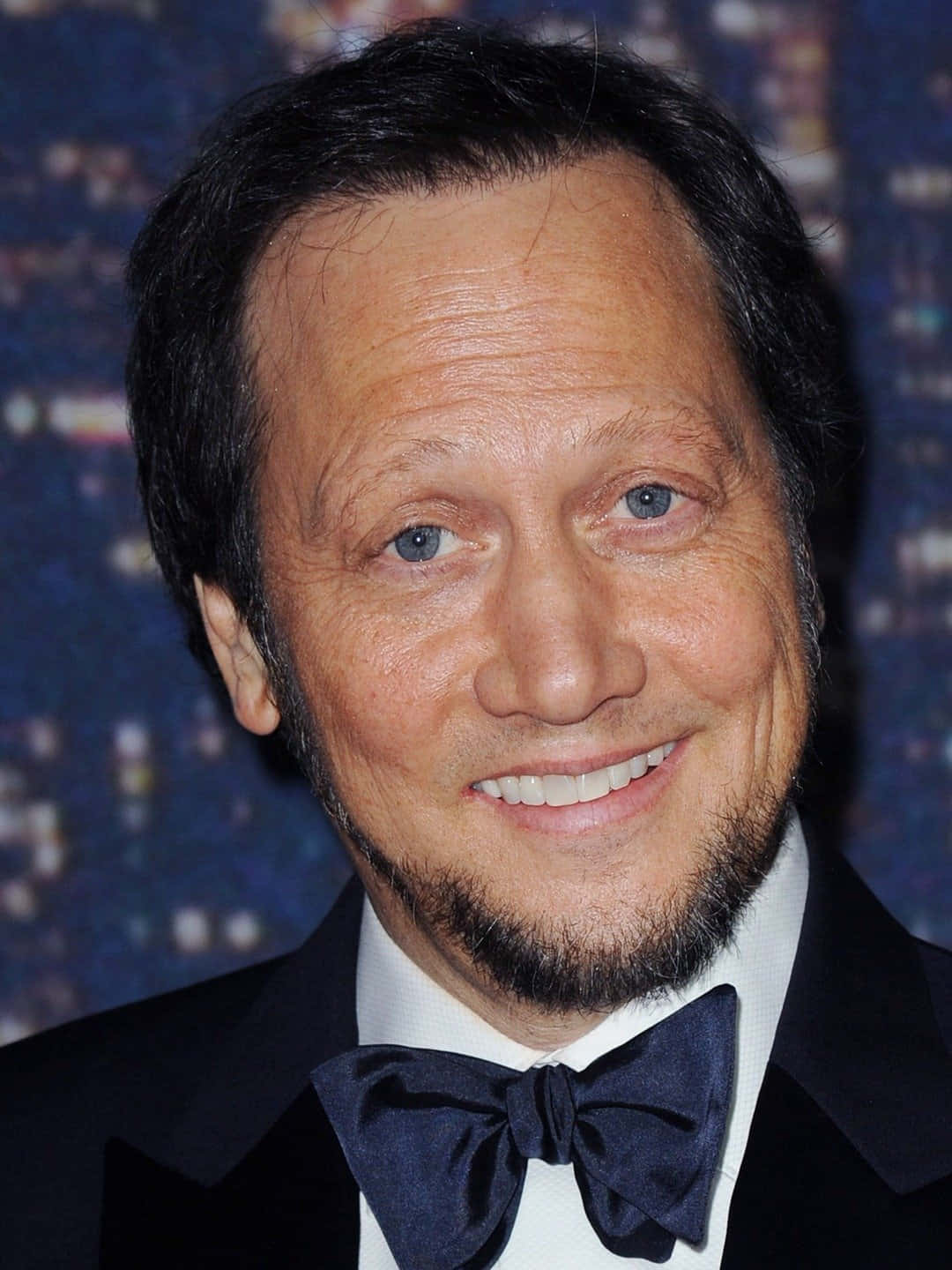 actor 桌布 壁紙 — 一個微笑男士穿著黑色禮服和蝴蝶結的頭像特寫，背景是模糊的城市景觀。