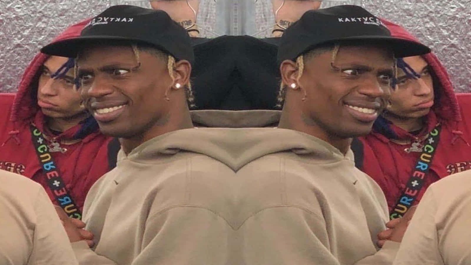 Travis Scott Funny 桌布 壁紙 — 一個微笑男子在米色連帽衫和黑色帽子中的鏡像自拍，周圍是其他穿紅色連帽衫的人。
