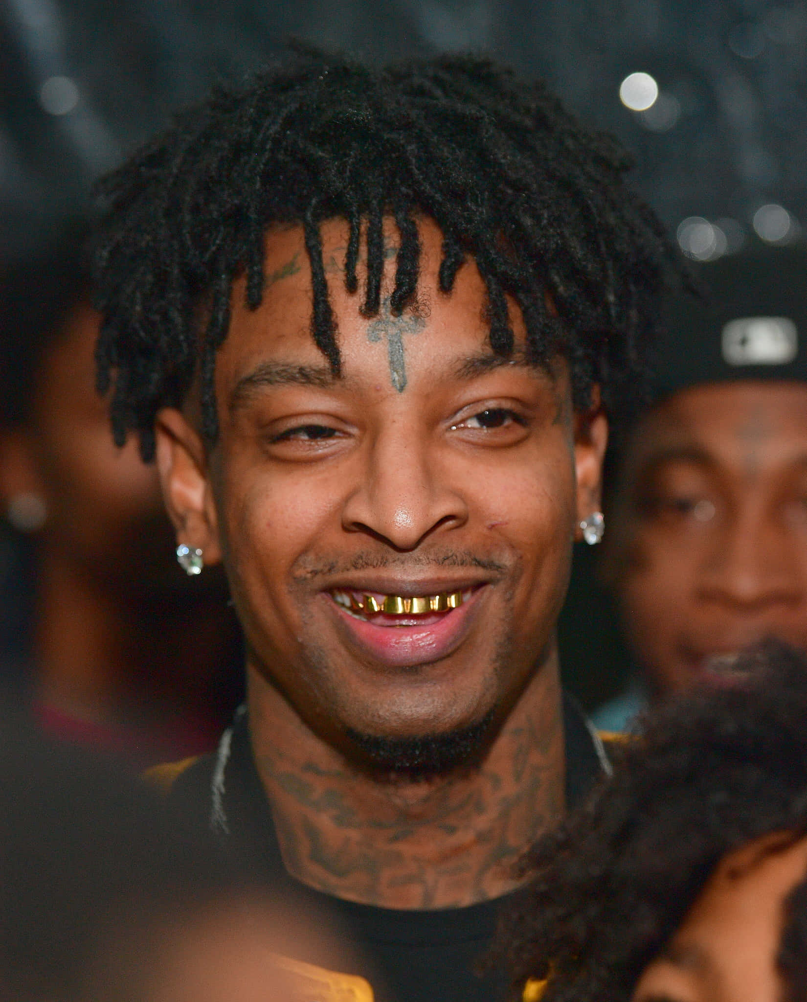 21 Savage 桌布 壁紙 — 一個微笑男子的特寫肖像，他有辮子頭、金牙套，額頭上有一個十字架刺青。