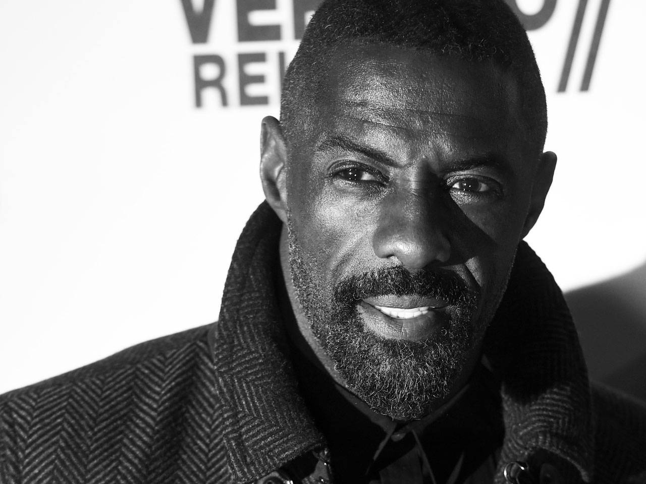 Celebrity 桌布 壁紙 — 一個微笑留鬍鬚的男人穿著人字紋大衣，在品牌背景前的黑白特寫肖像。
