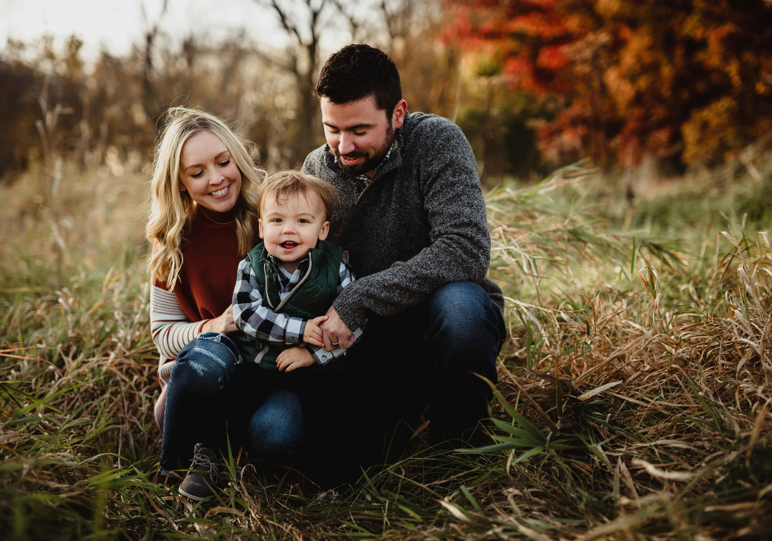 Fall Family 桌布 壁紙 — 一個微笑的三口之家在溫暖的秋光下，一起坐在高高的草叢中。