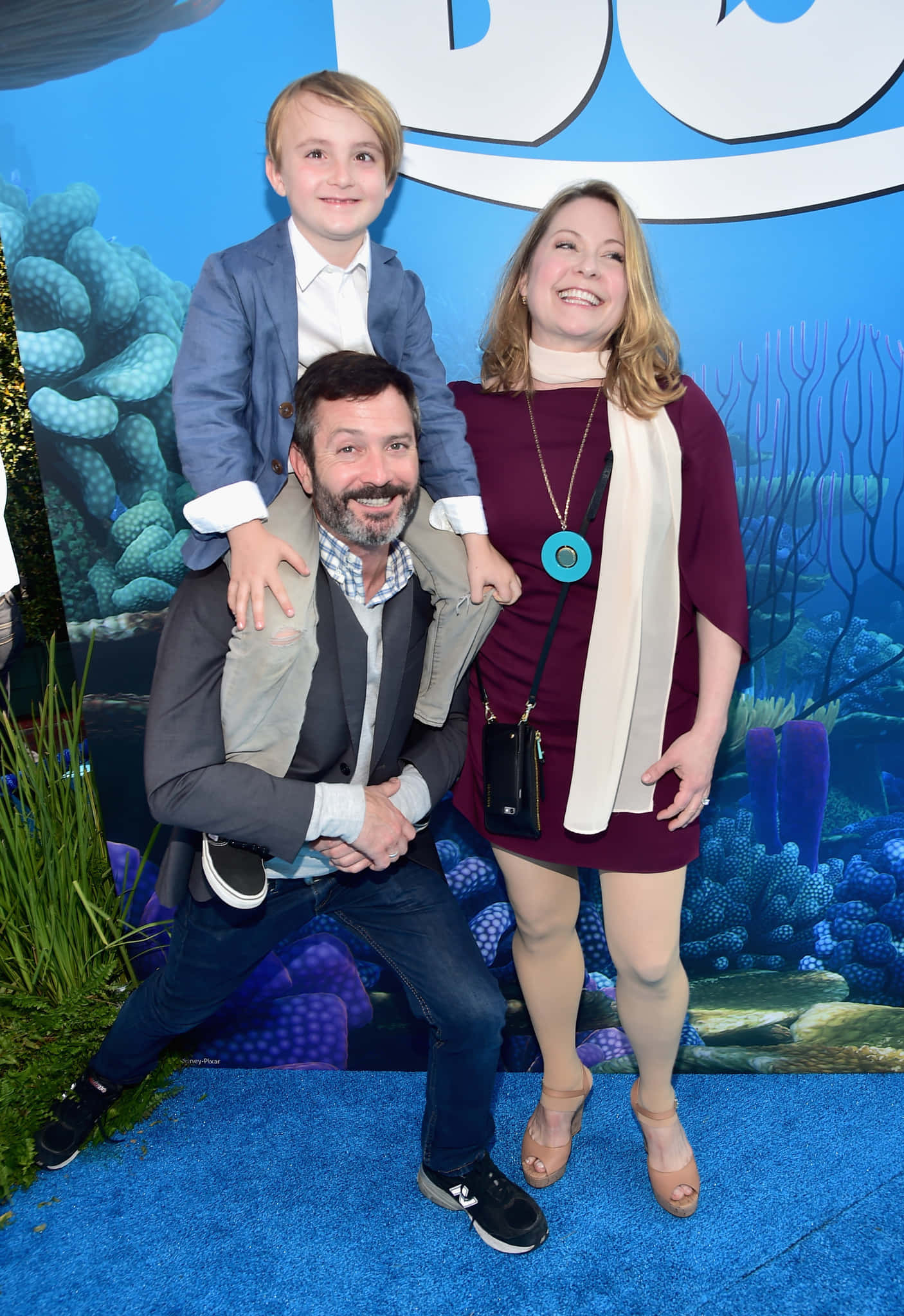 thomas lennon 桌布 壁紙 — 一個微笑的三口之家在藍色地毯上擺姿勢，背景是充滿活力的海底主題，有珊瑚和海洋生物。