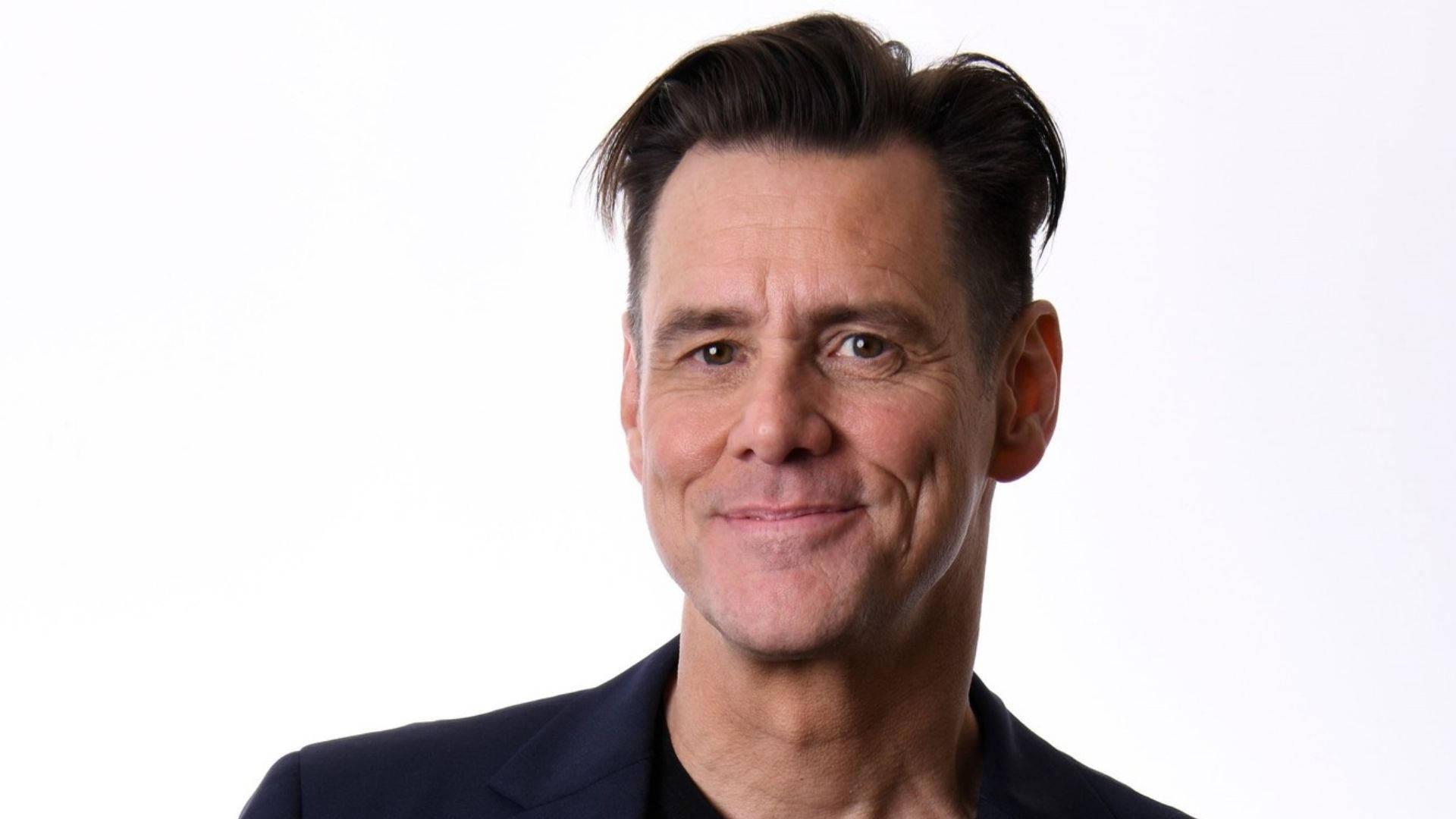 Jim Carrey 桌布 壁紙 — 一個微笑的中年男子特寫肖像，擁有造型深色頭髮，穿著深色西裝，背景為純白色。