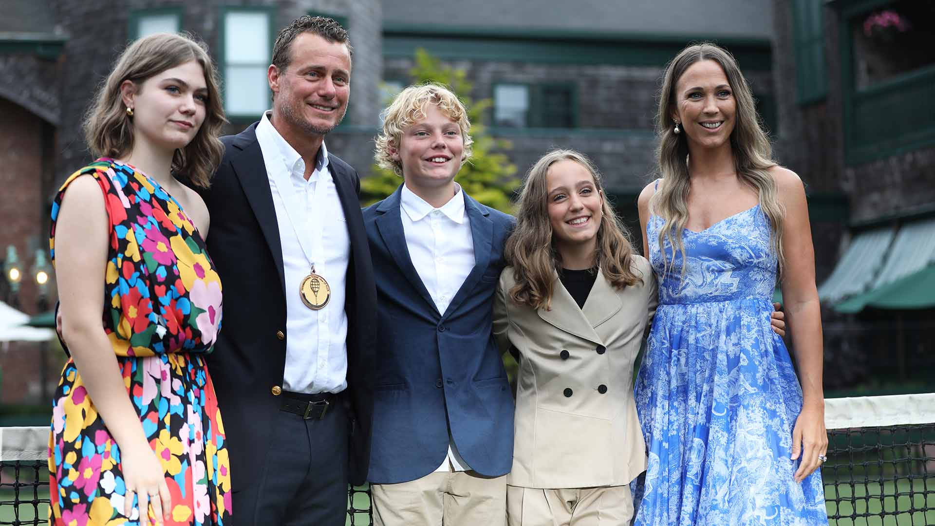 Family 桌布 壁紙 — 一個微笑的五人家庭在戶外磚砌建築前穿著色彩繽紛的正裝一起擺姿勢。
