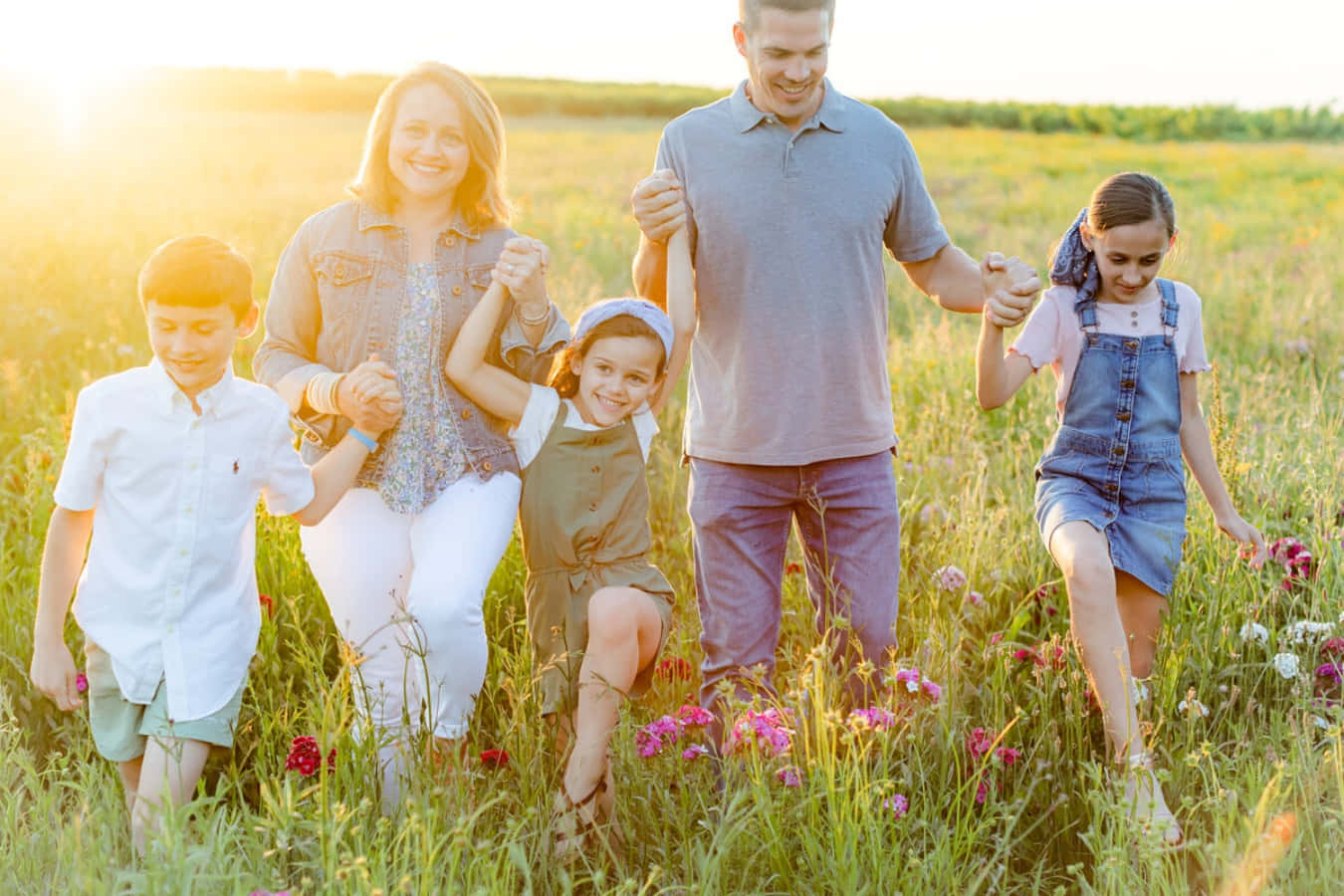 Spring Family 桌布 壁紙 — 一個微笑的五口之家手牽手走過陽光明媚、開滿野花的草地，正值黃金時刻。