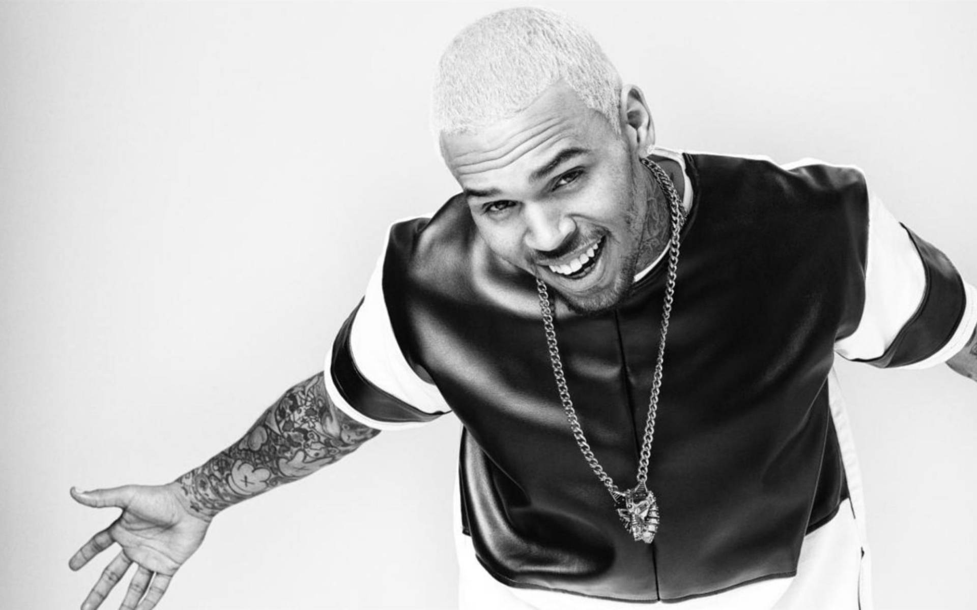 Chris Brown 桌布 壁紙 — 一個微笑的光頭男子黑白肖像，手臂有刺青，穿著皮夾克和鏈條。