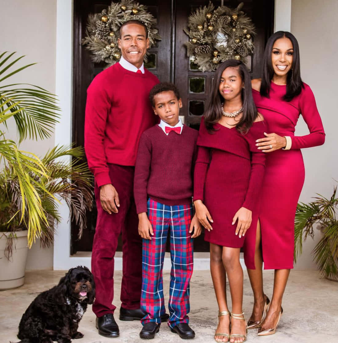 Black Family 桌布 壁紙 — 一個微笑的四口之家和他們的黑狗在裝飾好的前門前穿著節日紅色服裝擺姿勢。