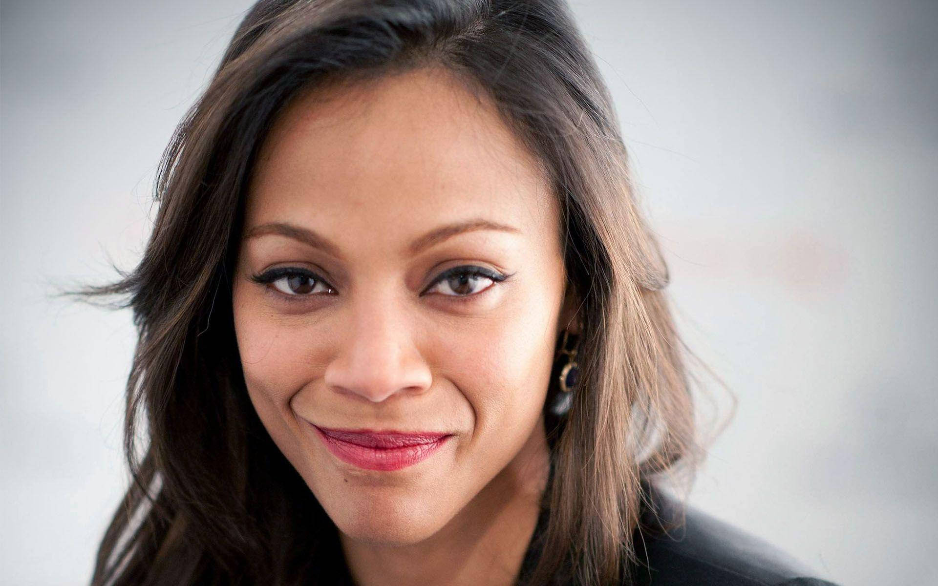 Zoe Saldana 桌布 壁紙 — 一個微笑的女人特寫肖像，深色頭髮和紅色唇膏，背景是柔和的灰色。