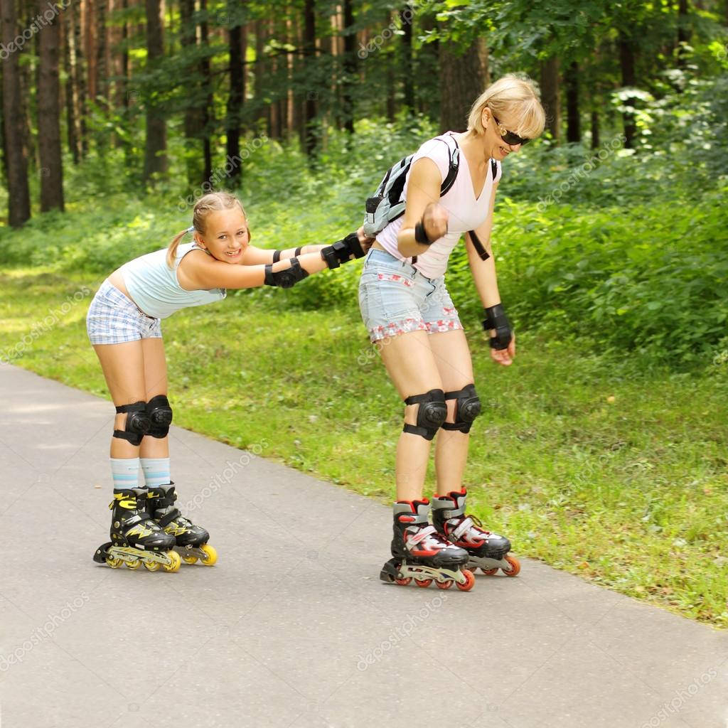 skating 桌布 壁紙 — 一個微笑的女孩幫助她的媽媽在森林小徑上保持溜冰鞋的平衡。