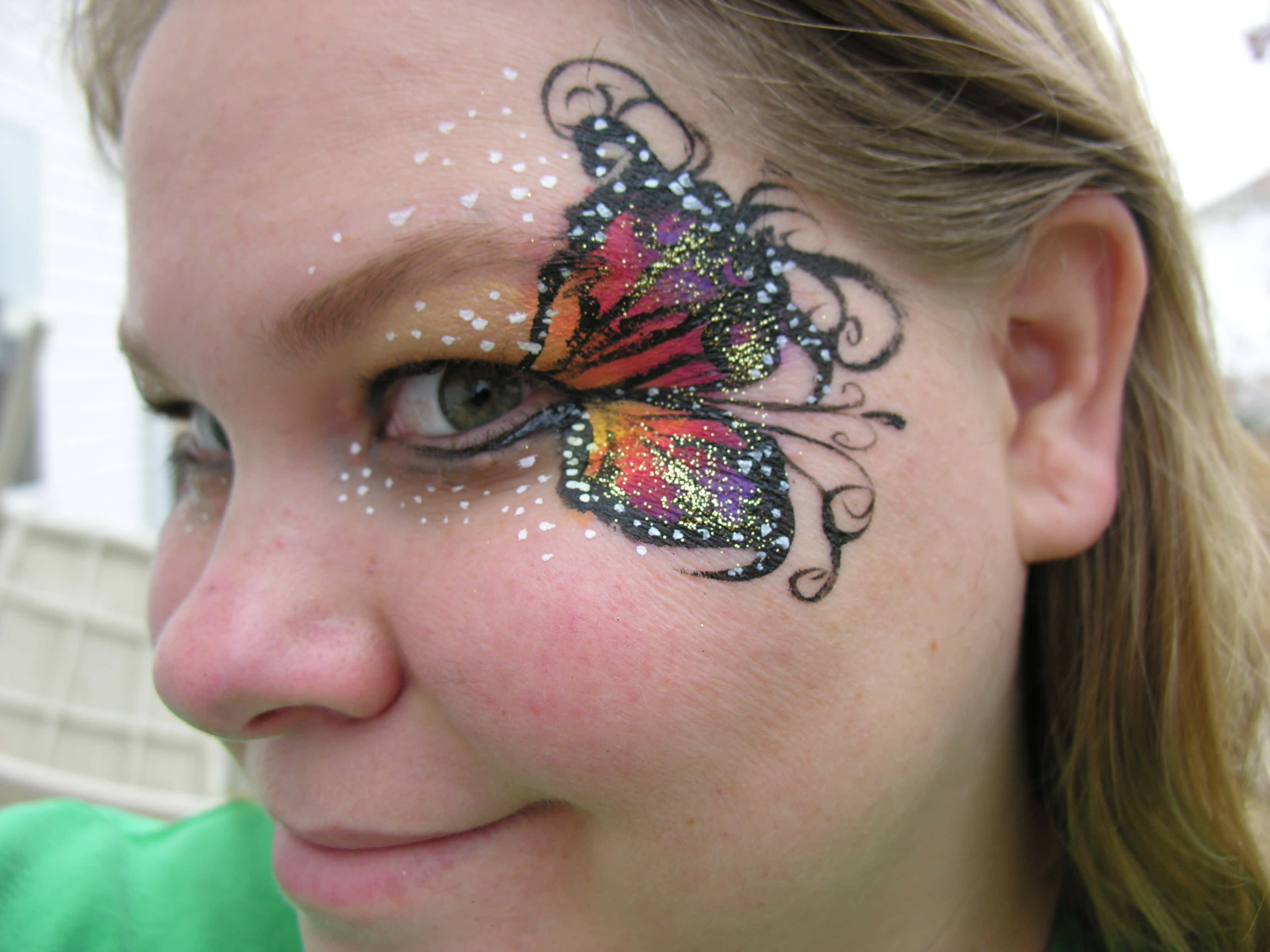 Butterfly Face Painting 桌布 壁紙 — 一個微笑的女孩的特寫，臉頰上畫著閃閃發光的彩色蝴蝶，眼睛周圍有白色圓點。