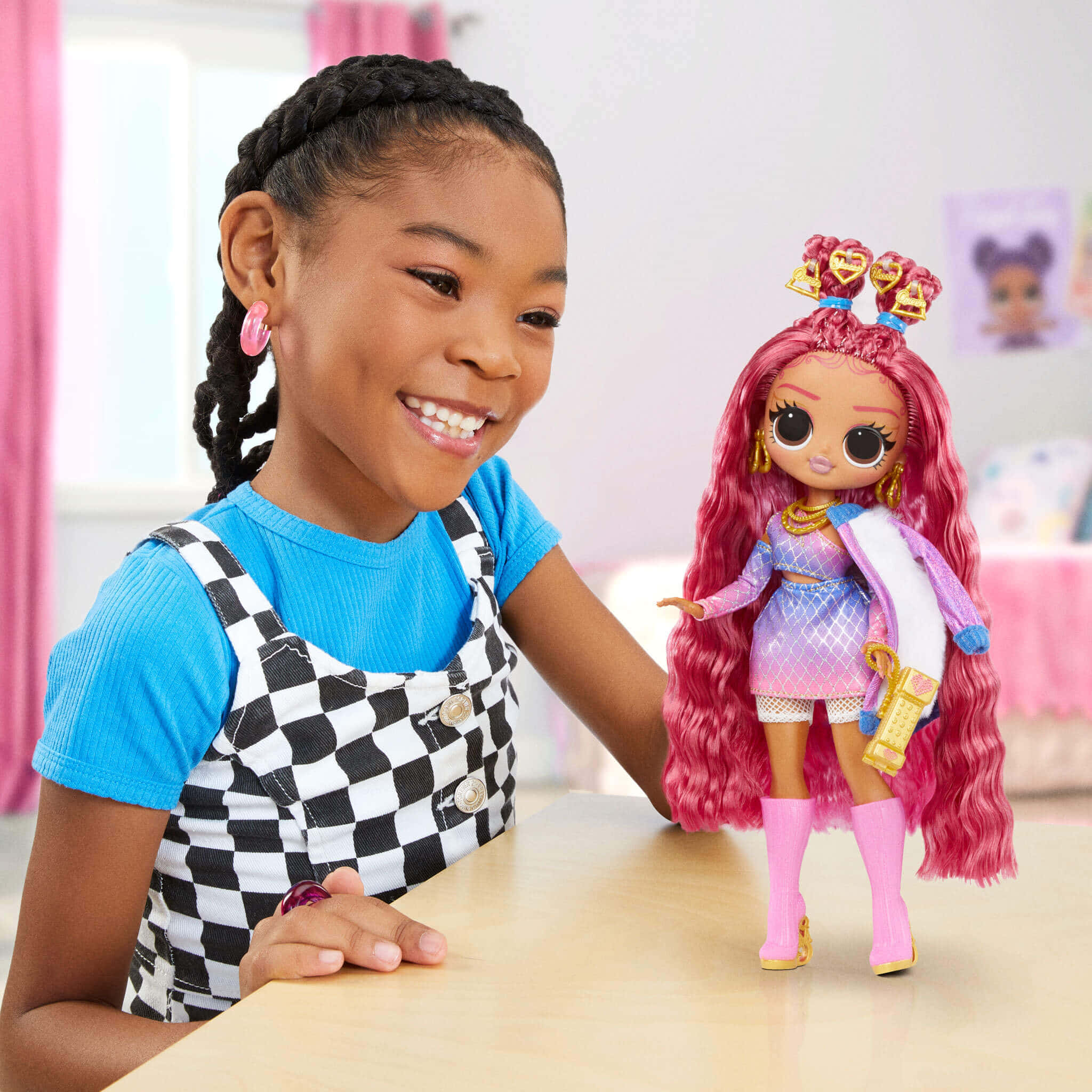 Lol Dolls 桌布 壁紙 — 一個微笑的女孩穿著格紋吊帶褲坐在桌旁，欣賞她衣著鮮豔、粉紅色頭髮的娃娃。
