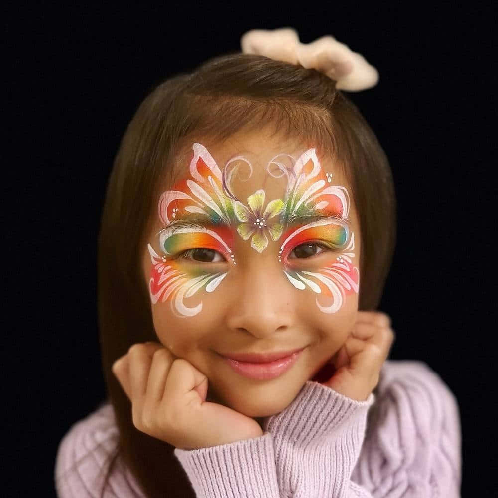 Butterfly Face Painting 桌布 壁紙 — 一個微笑的孩子，臉上畫著鮮豔的彩虹蝴蝶圖案，戴著白色蝴蝶結，背景為黑色。