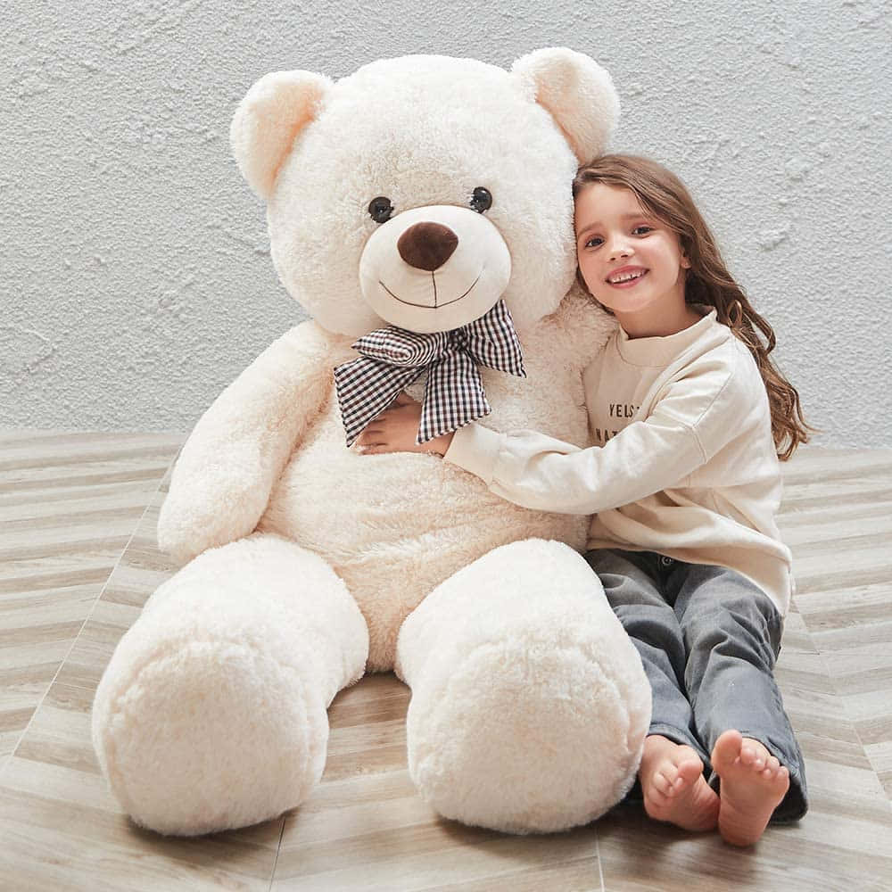 Cute Teddy 桌布 壁紙 — 一個微笑的孩子擁抱一隻巨大的毛絨奶油色泰迪熊，繫著格子蝴蝶結，背景是紋理牆壁。
