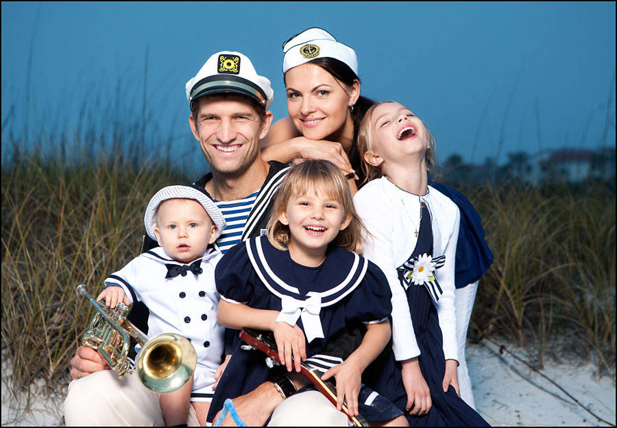 Family 桌布 壁紙 — 一個微笑的家庭穿著水手服在沙灘上一起擺姿勢，身後有沙丘草，頭頂是清澈的藍天。