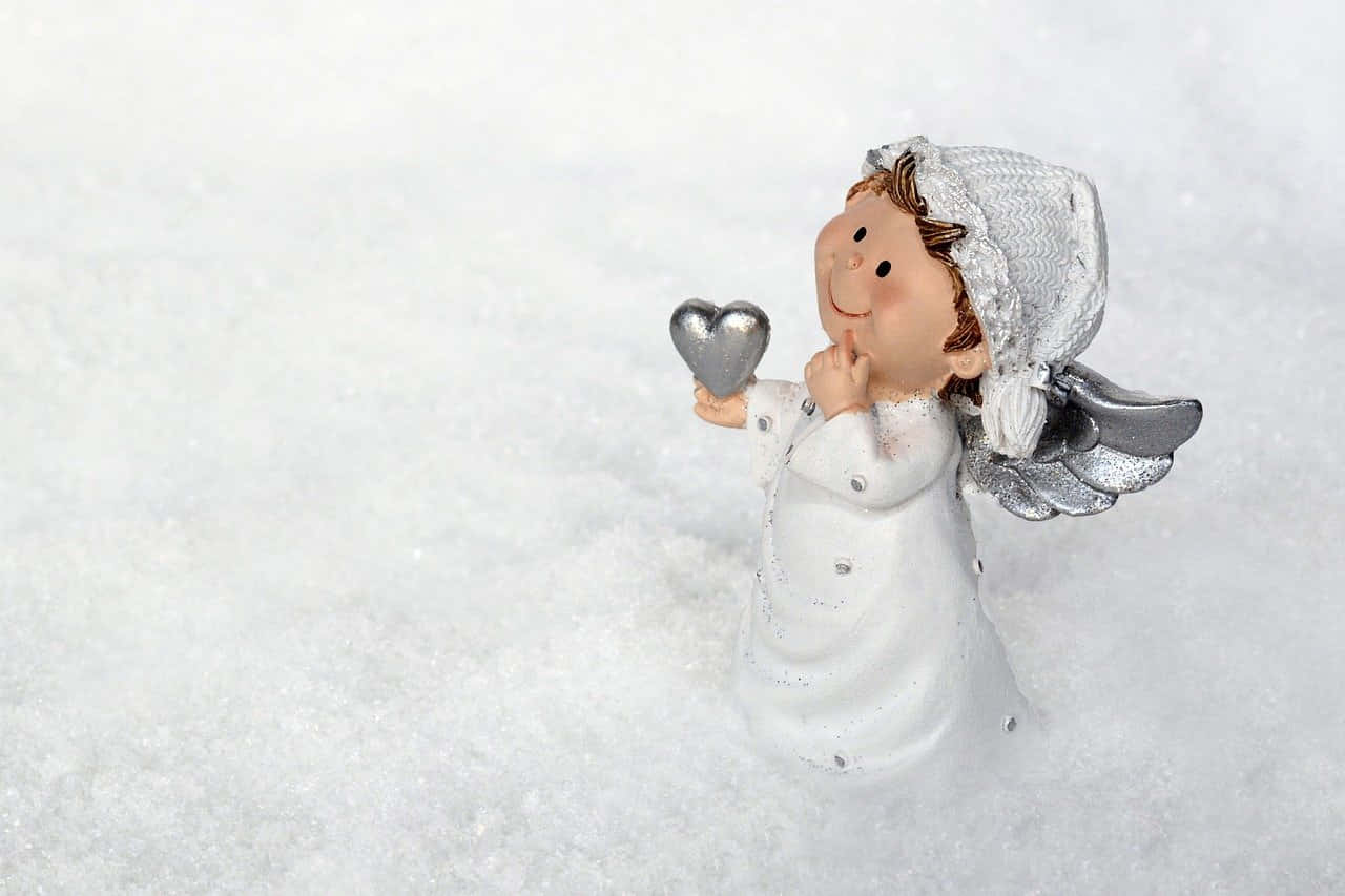 Snow Angel 桌布 壁紙 — 一個微笑的小天使雕像，帶有銀色翅膀和一顆心，安放在潔白的新雪中。