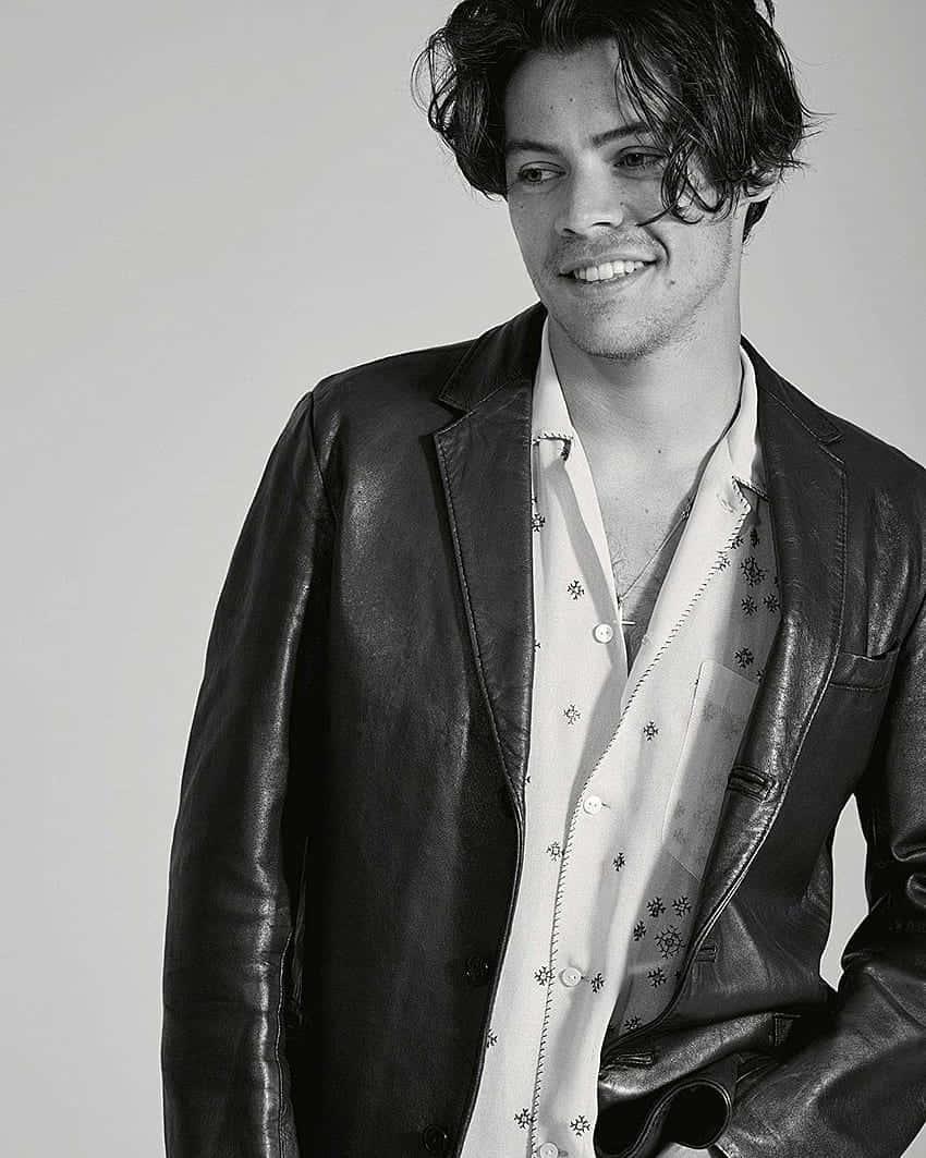 Harry Styles Black And White 桌布 壁紙 — 一個微笑的年輕男子穿著皮夾克和圖案襯衫，在純色背景前的黑白肖像。
