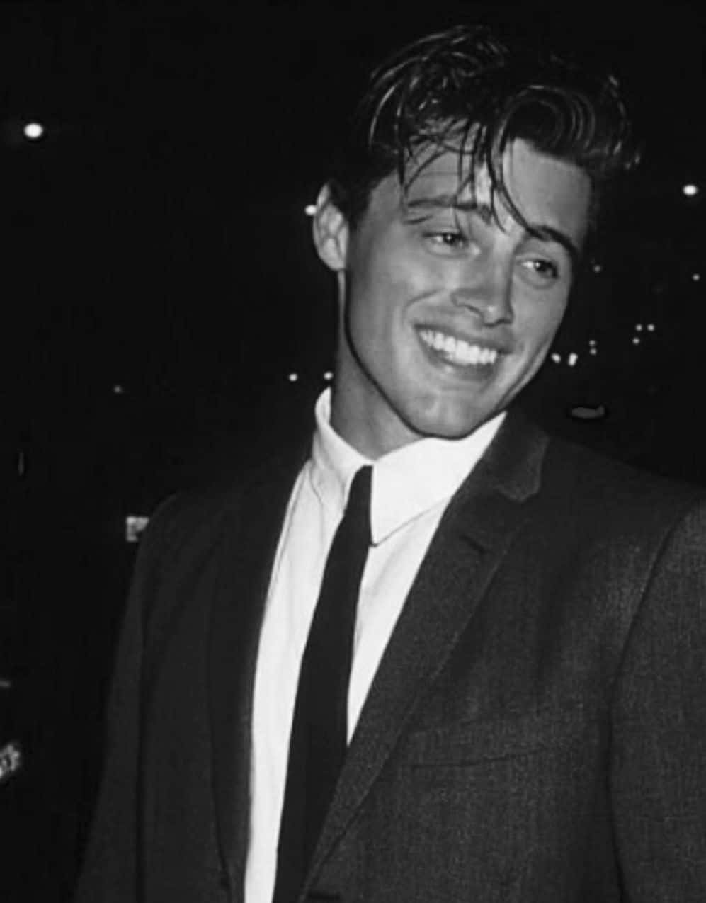 Matt Leblanc 桌布 壁紙 — 一個微笑的年輕男子穿著西裝，在黑暗背景與模糊燈光下的黑白肖像。