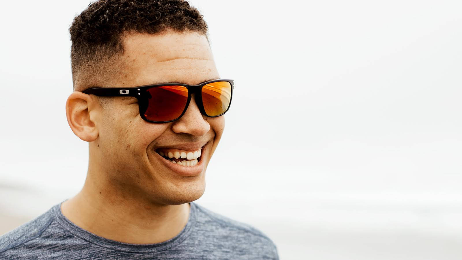 Sunglasses 桌布 壁紙 — 一個微笑的捲髮男子戴著黑色太陽眼鏡，橙色鏡片，背景是明亮的白色。