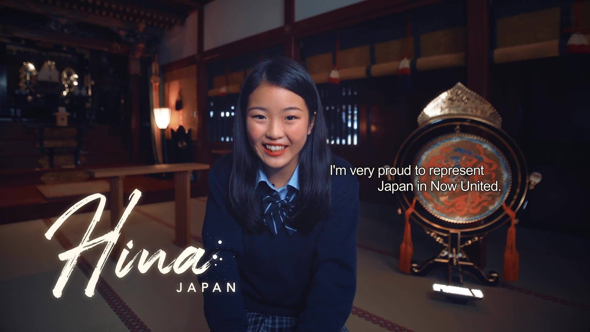Now 桌布 壁紙 — 一個微笑的日本女學生穿著校服坐在傳統木房間裡，旁邊有一個裝飾鼓。