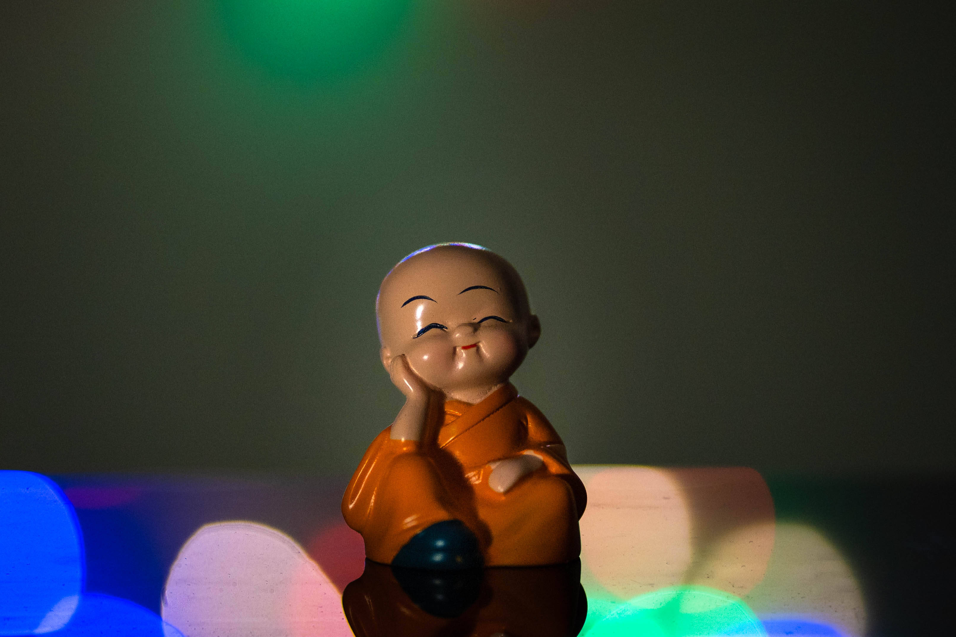 Dolls 桌布 壁紙 — 一個微笑的橙色長袍佛像，坐在色彩繽紛的散景背景前沉思。