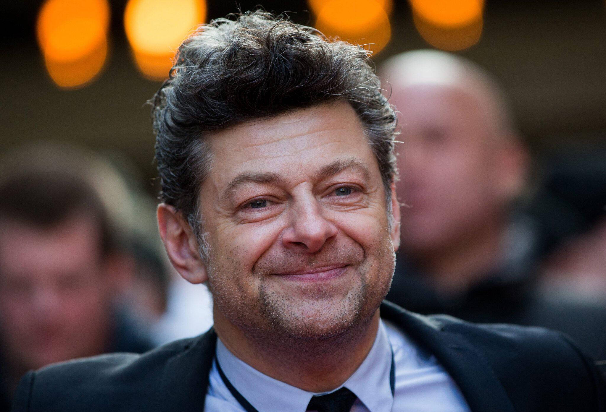 actor 桌布 壁紙 — 一個微笑的深色捲髮男士穿著西裝打領帶的特寫肖像，背景是溫暖的散景燈光模糊效果。