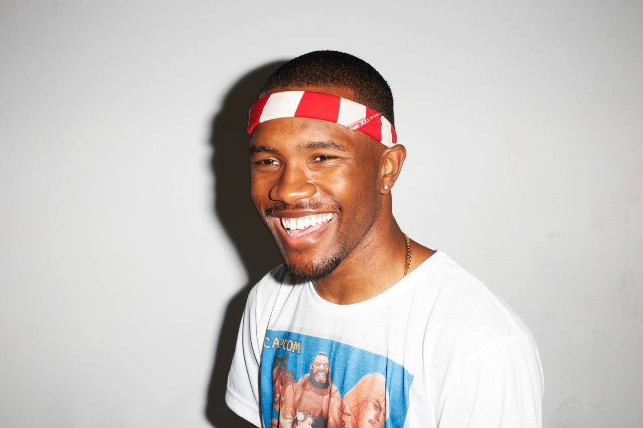 Frank Ocean 桌布 壁紙 — 一個微笑的男人，戴著紅白相間的頭帶，穿著圖案T恤，背景是純灰色的牆壁。