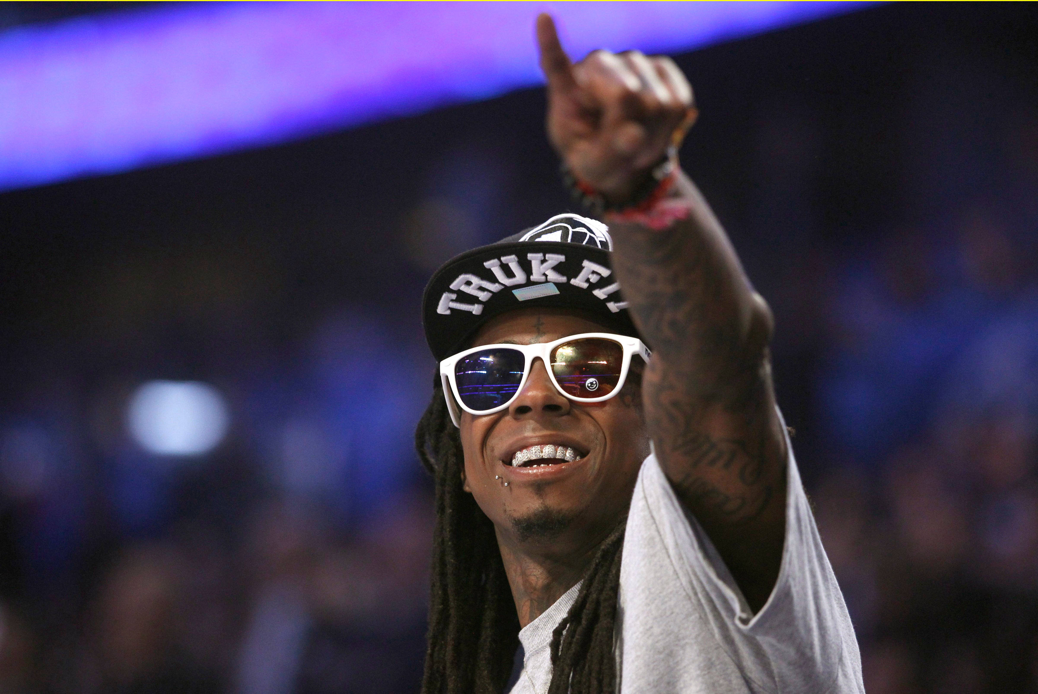 Lil Wayne 桌布 壁紙 — 一個微笑的男人，梳著辮子頭，戴著白色太陽眼鏡，在紫色舞台燈光下的演唱會中向上指。