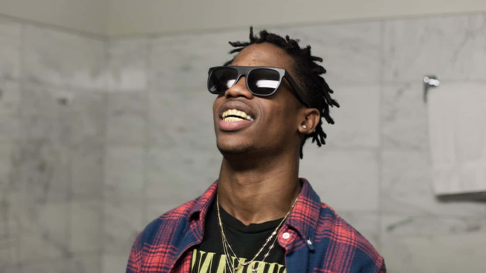 Travis Scott Funny 桌布 壁紙 — 一個微笑的男人，留著辮子頭和戴著太陽眼鏡，在鋪有大理石瓷磚的浴室裡開懷大笑。
