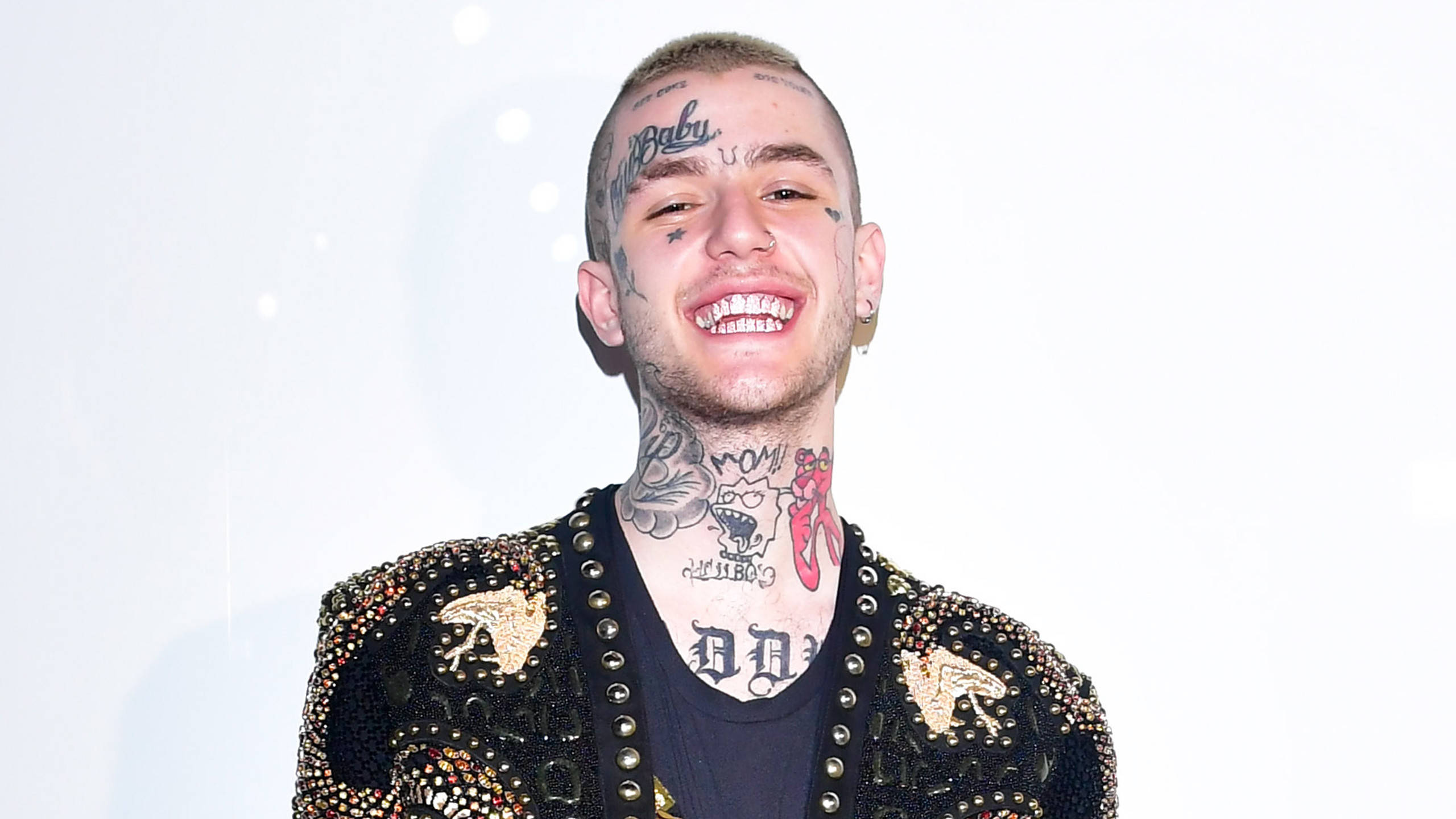 Peep 桌布 壁紙 — 一個微笑的男人，臉上和脖子上有刺青，穿著一件帶有鉚釘的黑色外套，背景是明亮的白色。