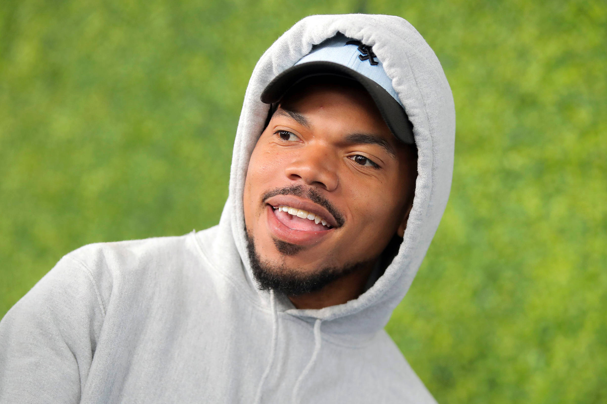 chance 桌布 壁紙 — 一個微笑的男人，身穿灰色連帽衫和帽子，背景是充滿活力的綠色模糊背景。