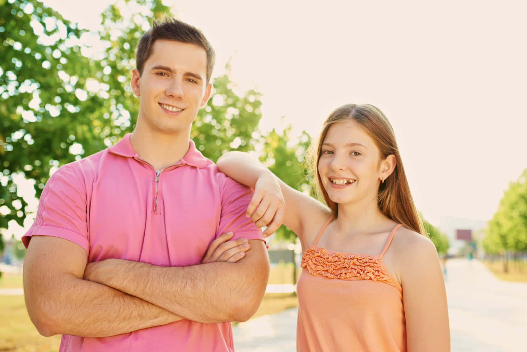 Brother And Sister 桌布 壁紙 — 一個微笑的男人和女孩在戶外陽光下交叉雙臂並搭肩合照。