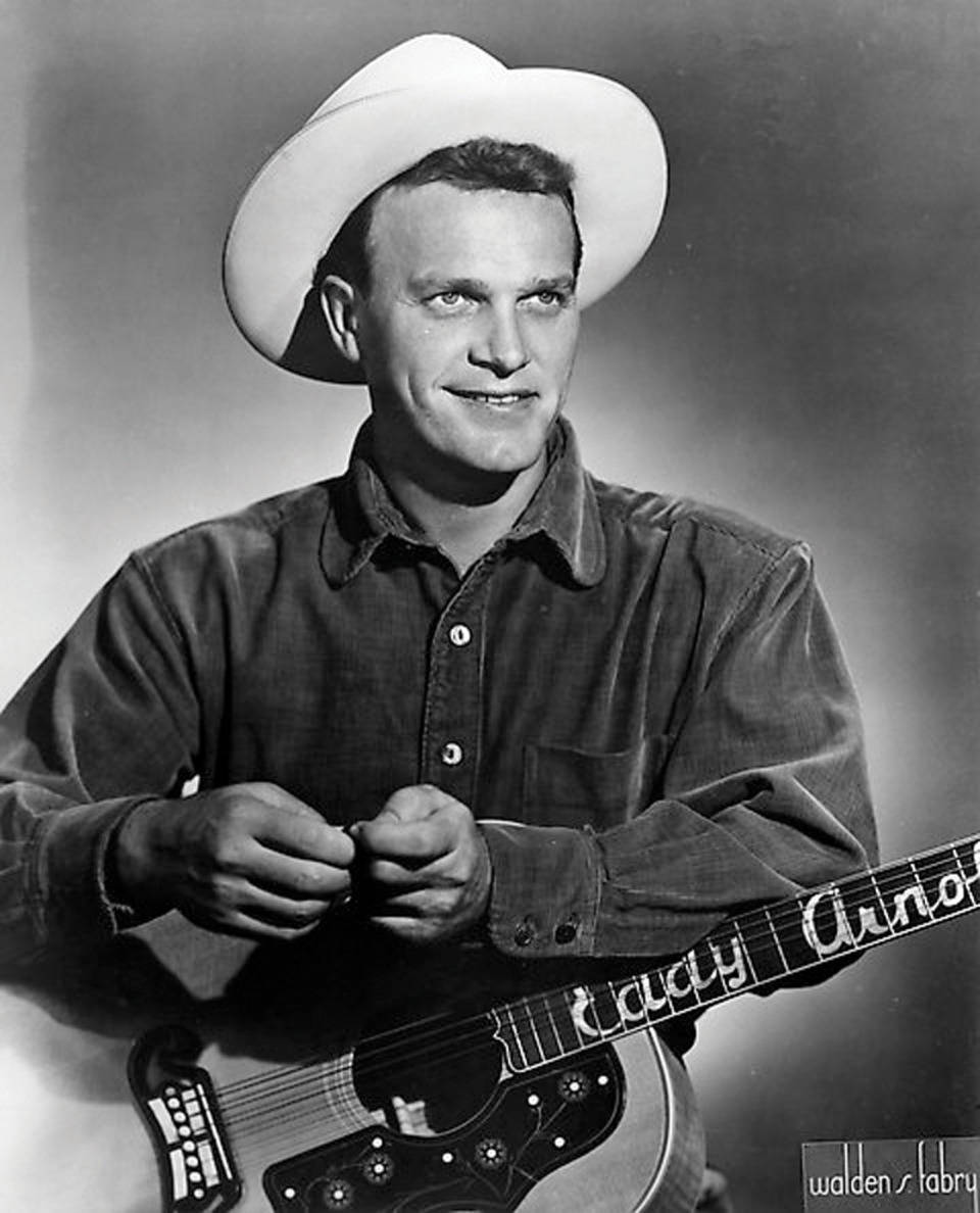 Eddy Arnold 桌布 壁紙 — 一個微笑的男人戴著白色牛仔帽，拿著一把琴頸上寫有「Lucky Arno」的吉他，背景是柔和的攝影棚。