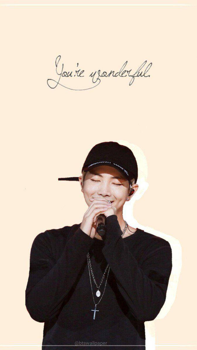 Namjoon 桌布 壁紙 — 一個微笑的男人戴著黑色帽子和襯衫，在柔和的米色背景前拿著麥克風，上方有草書文字「你很棒」。