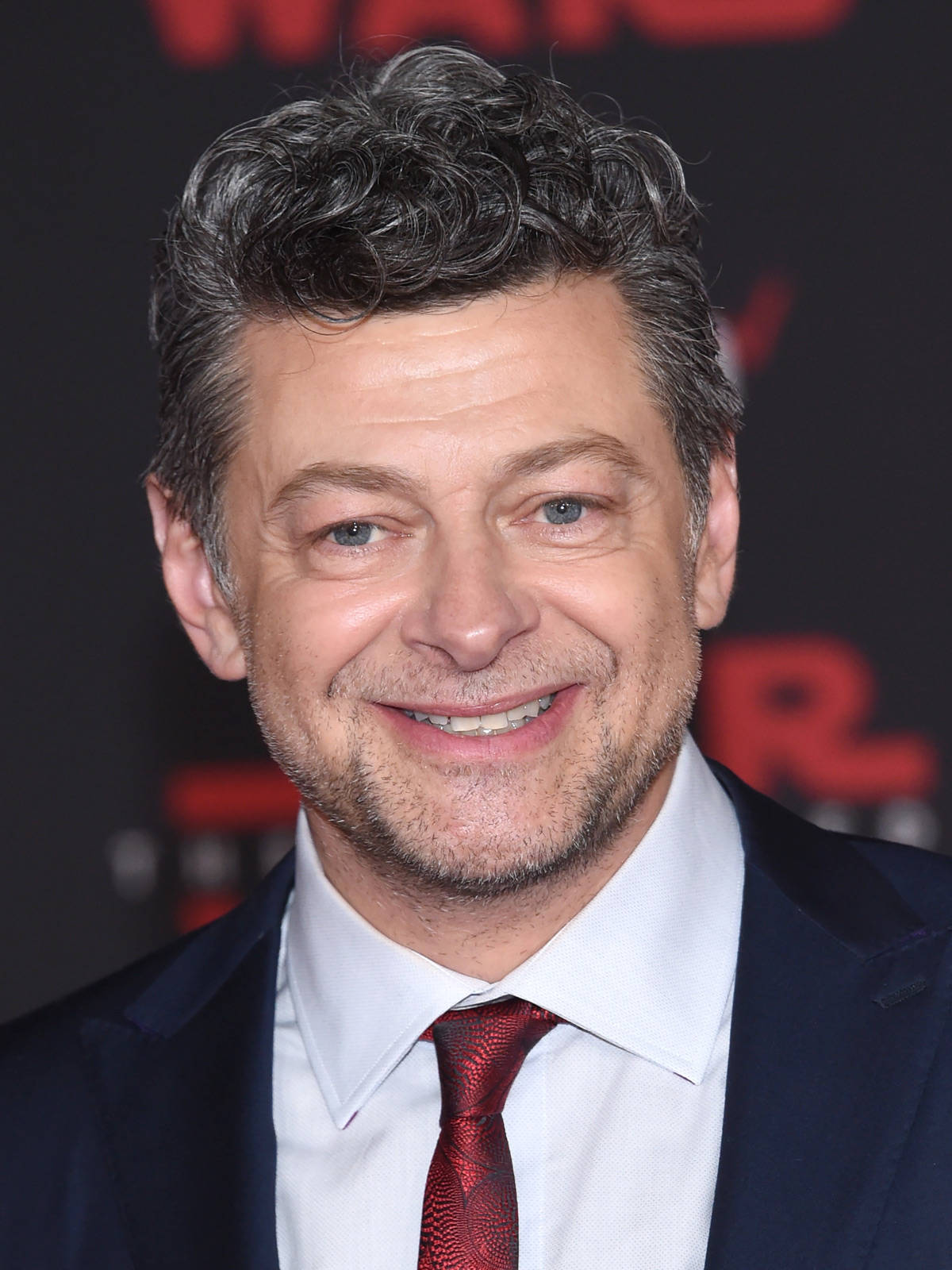 actor 桌布 壁紙 — 一個微笑的男人特寫肖像，頭髮花白，穿著深色西裝和紅色領帶，背景是模糊的紅色和黑色。