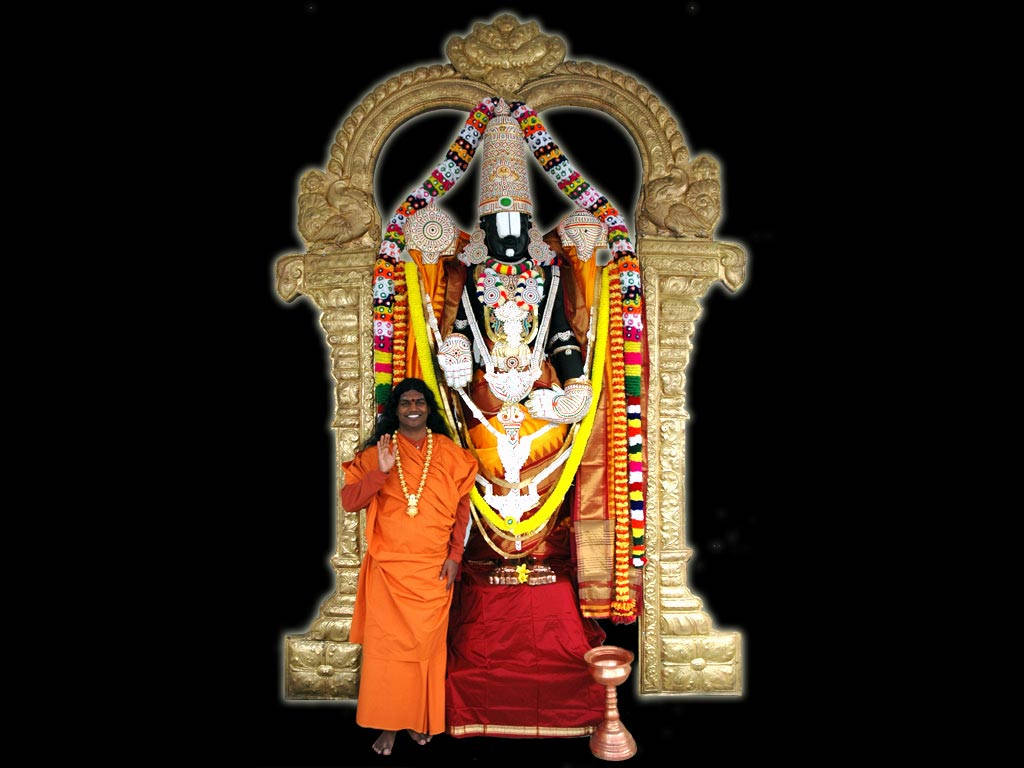 Hindu God 桌布 壁紙 — 一個微笑的男人穿著橙色長袍，站在一尊裝飾華麗的印度教神像前，神像被金色拱門框住，背景為黑色。