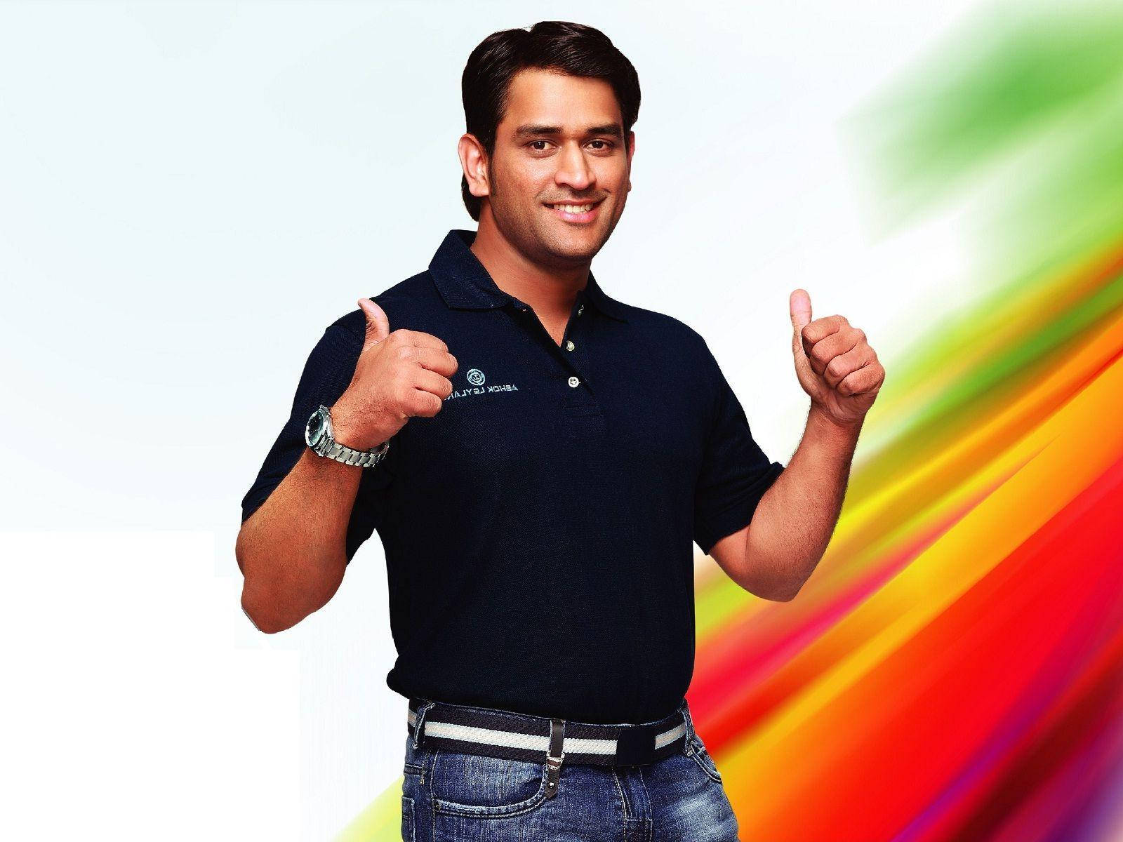 Ms Dhoni 桌布 壁紙 — 一個微笑的男人穿著深色Polo衫，在充滿活力的彩虹漸變背景前豎起兩個大拇指。